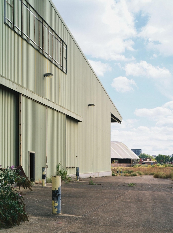 External facade of a green corrugated metal industrial warehouse building with concrete yards for production base crew parking, Love Locations Deptford.