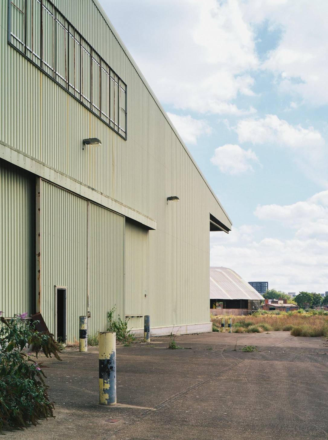 External facade of a green corrugated metal industrial warehouse building with concrete yards for production base crew parking, Love Locations Deptford.