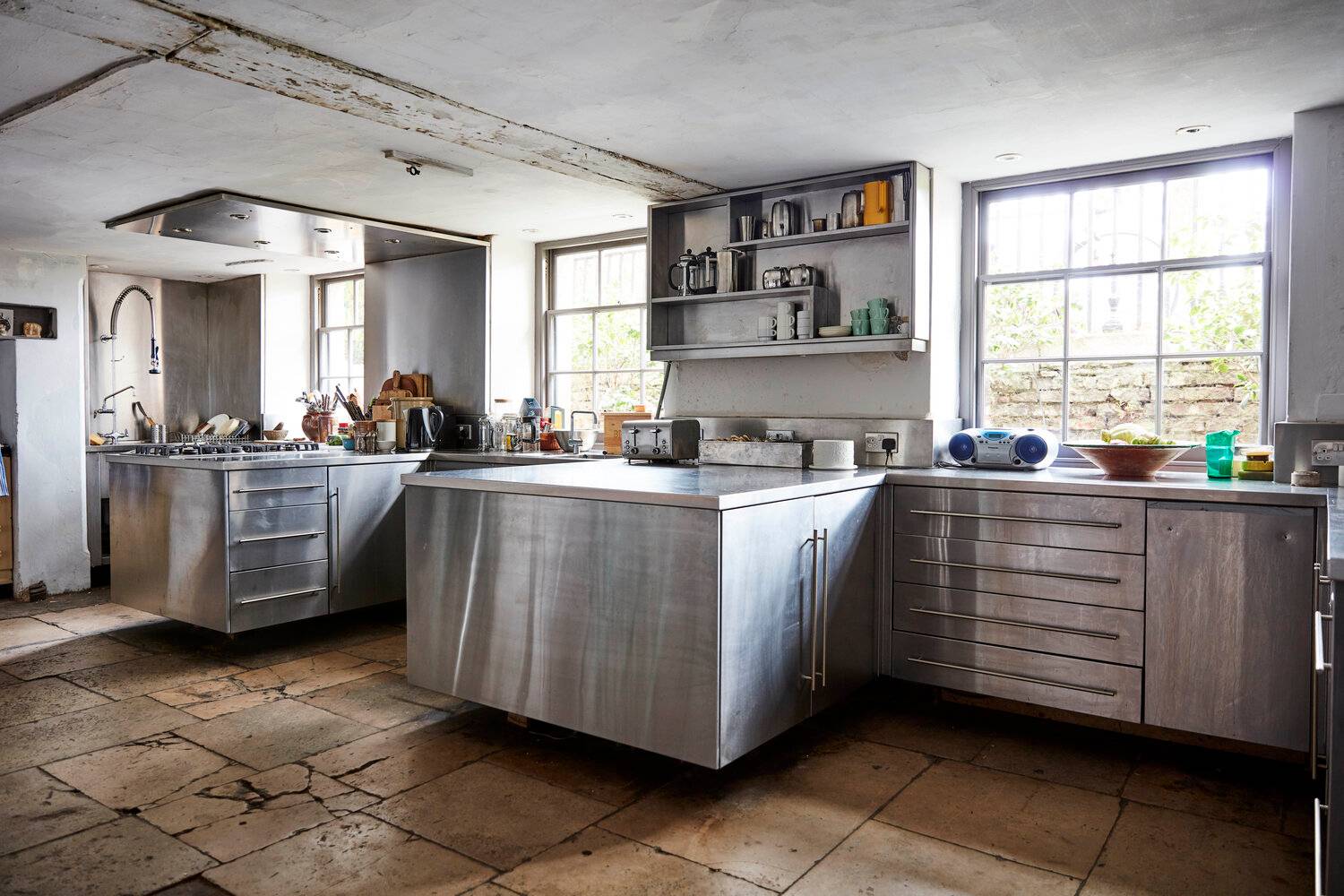 Stainless steel commercial kitchen island set in a rustic room with flagstone floors and dual sash windows, Love Locations SE8.
