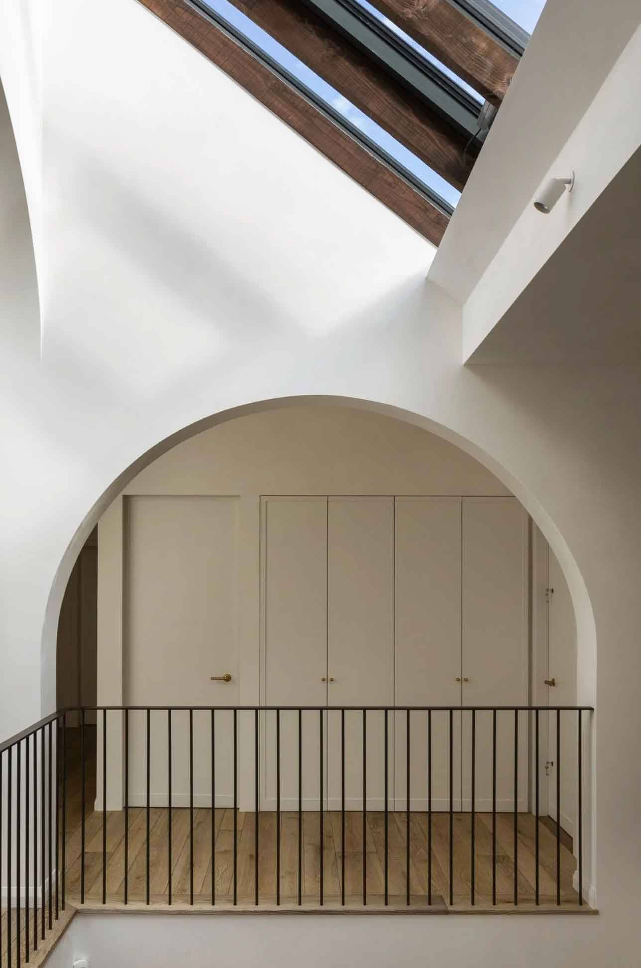 Architectural view of an upper landing archway framing minimalist built-in wardrobes under ceiling skylights, Love Locations.