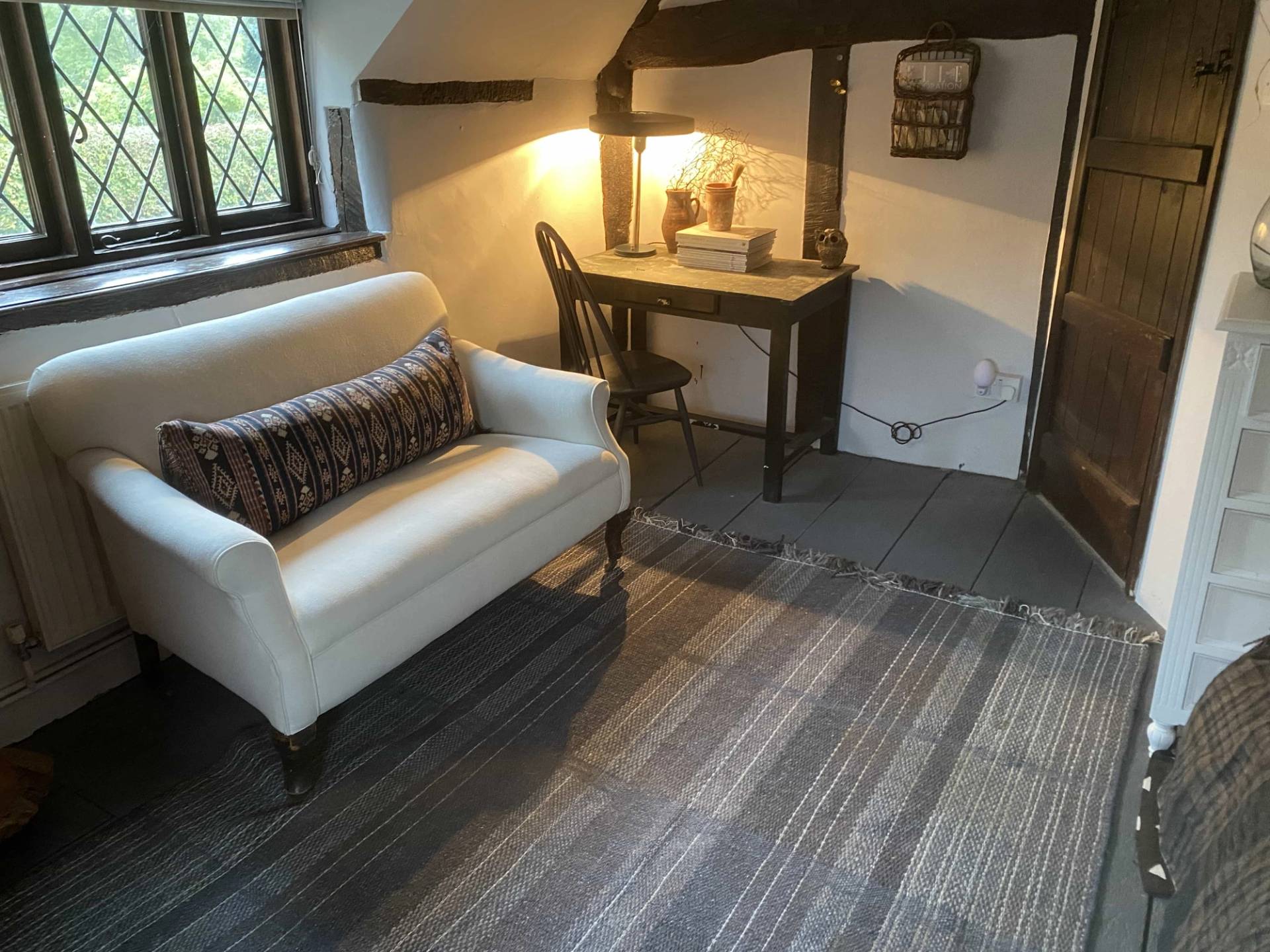 Intimate upstairs sitting room nook featuring a white sofa, a writing desk, and a small Queen Anne window overlooking the valley, Love Locations.