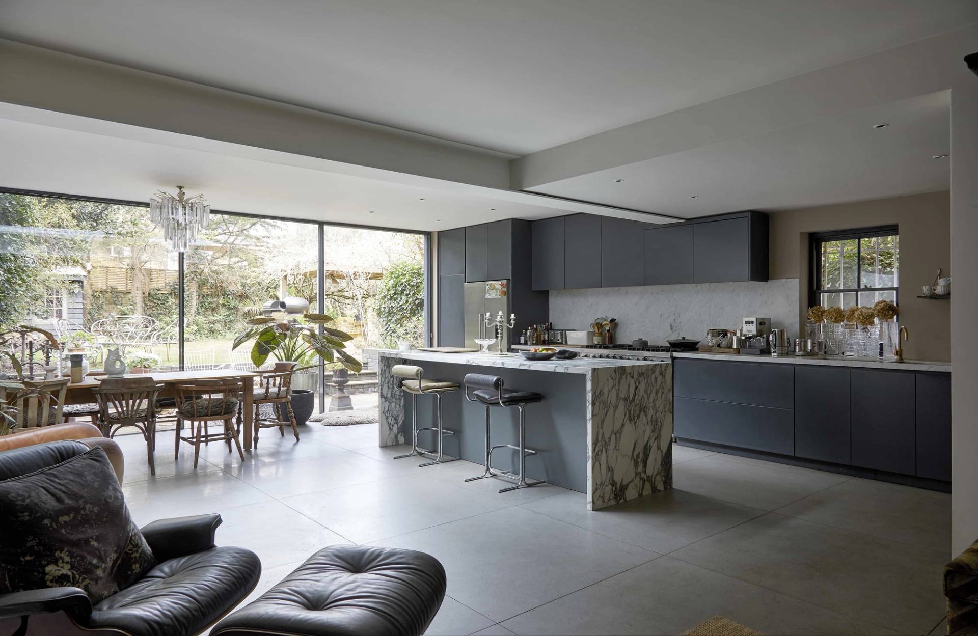 Contemporary open-plan kitchen featuring dark grey cabinets, waterfall marble island, and glass sliding doors, Love Locations N16.
