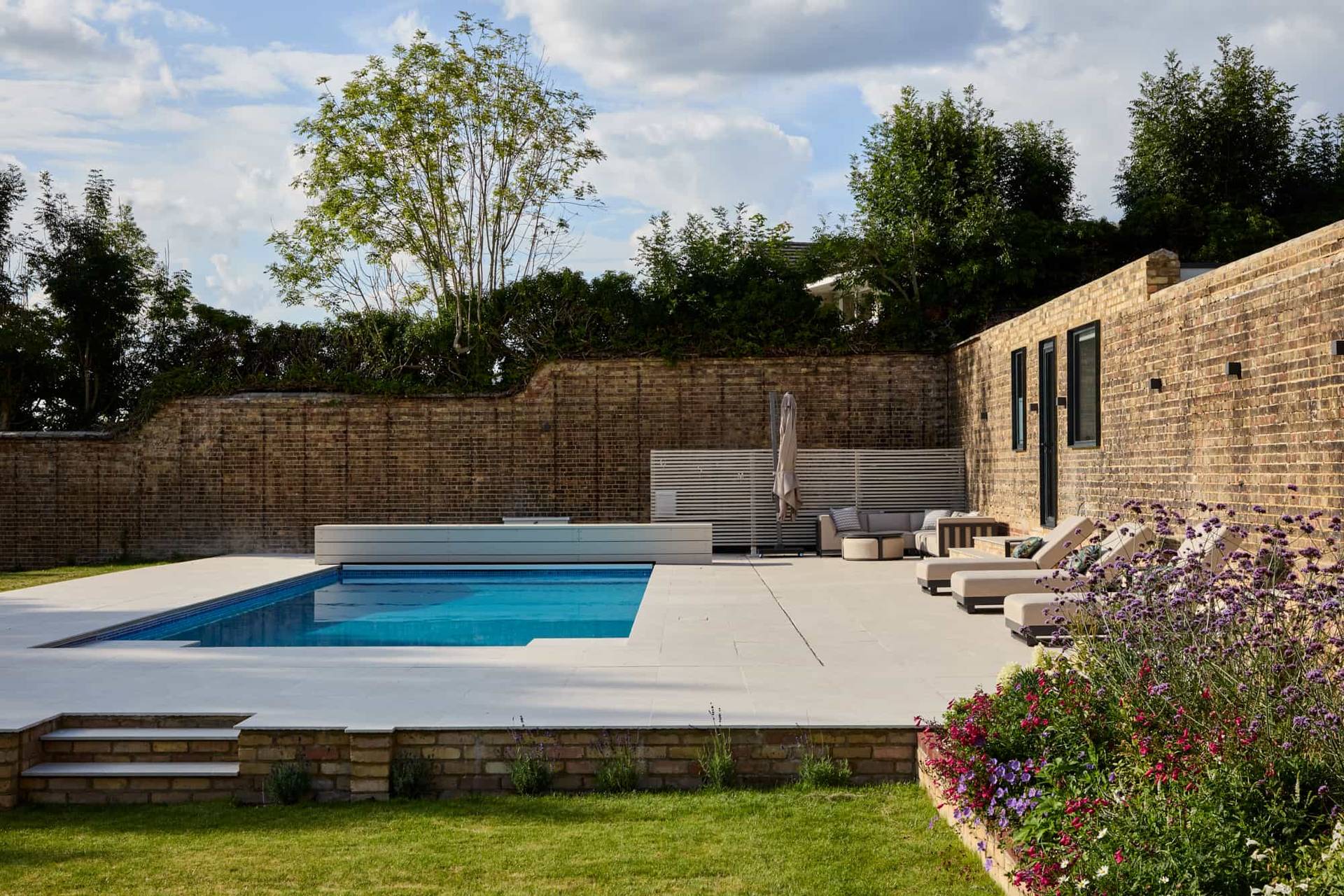 Paved poolside terrace and manicured lawn area overlooking a modern single-storey villa in Surrey, Love Locations.
