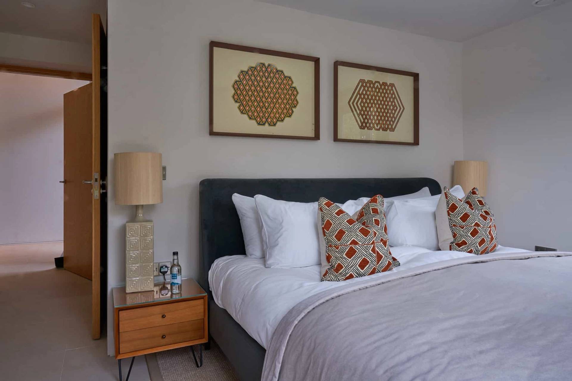 Master bedroom with a dark velvet upholstered bed, mid-century nightstands, and framed wall art, Love Locations SO21.