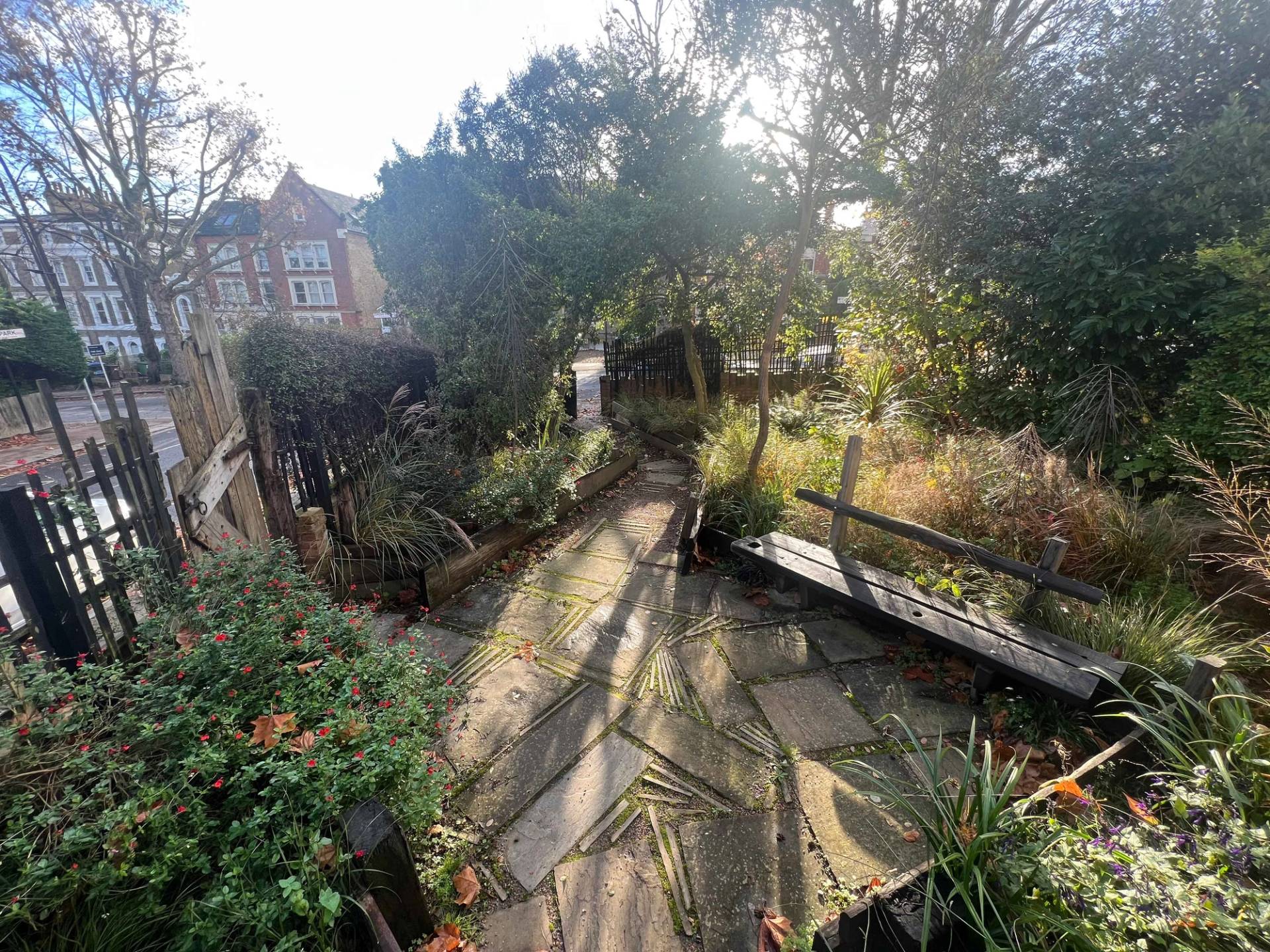 Sunlit garden terrace paved with stone slabs and surrounded by mature trees and garden foliage, Love Locations SE5.