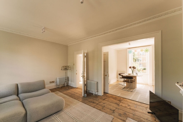 Wide perspective view looking from a bright living room across wooden floors toward a connected rear dining zone, Love Locations.