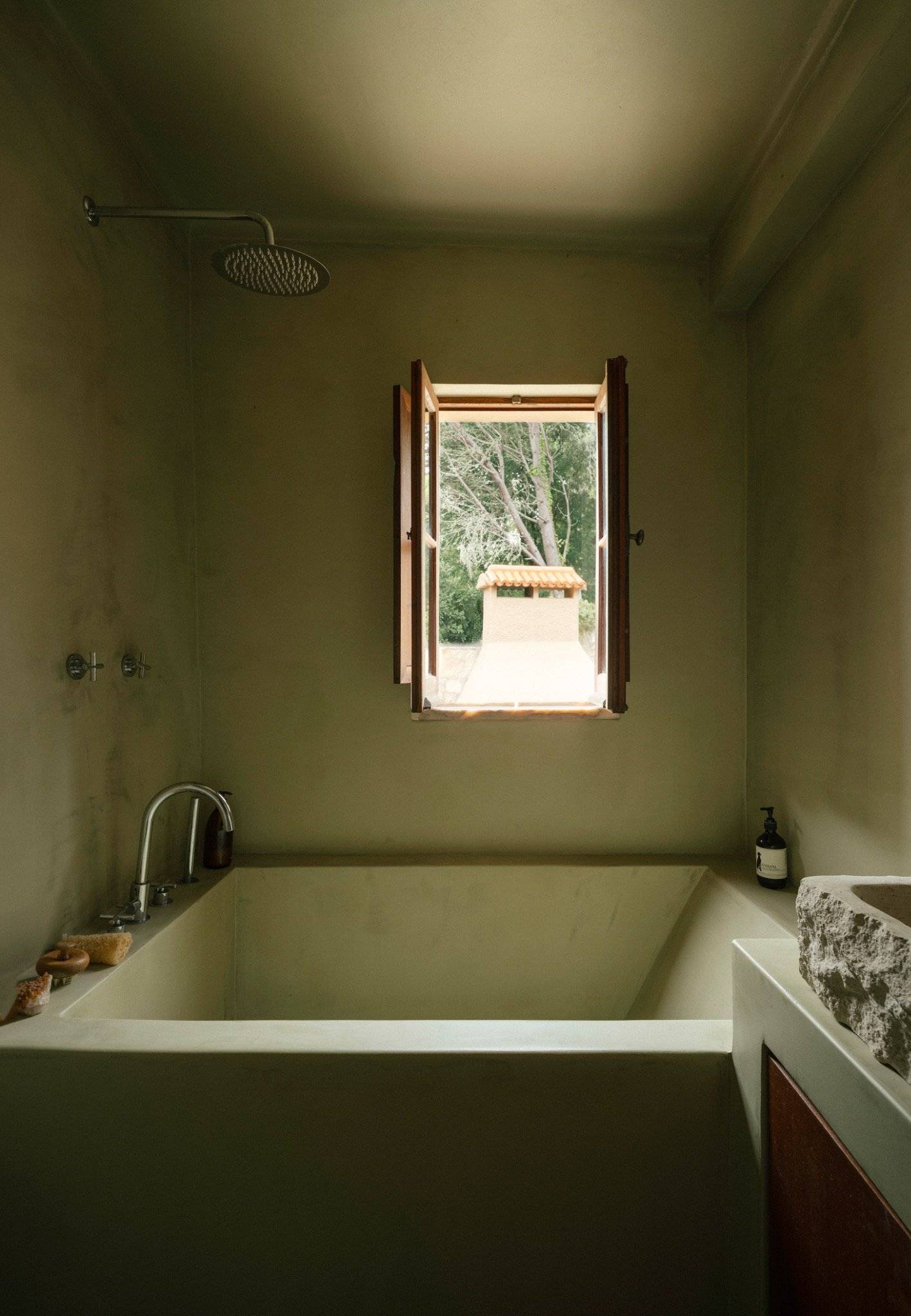 Olive green microcement bathroom with an integrated sunken bathtub and small view window, Love Locations 2705-064.