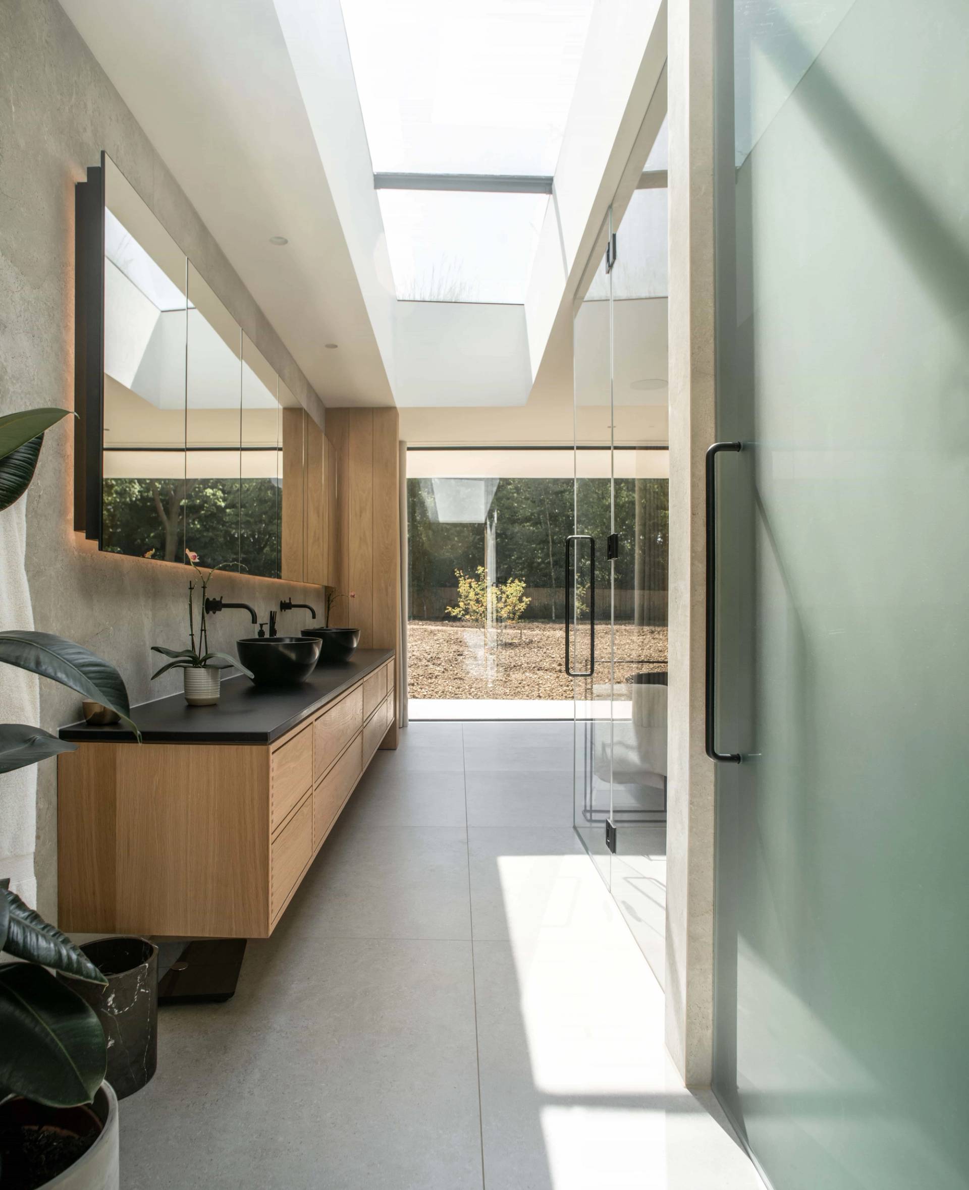 Designer ensuite bathroom vanity area with dual vessel sinks, modern black hardware, and bright natural light from architectural roof lanterns, Love Locations.