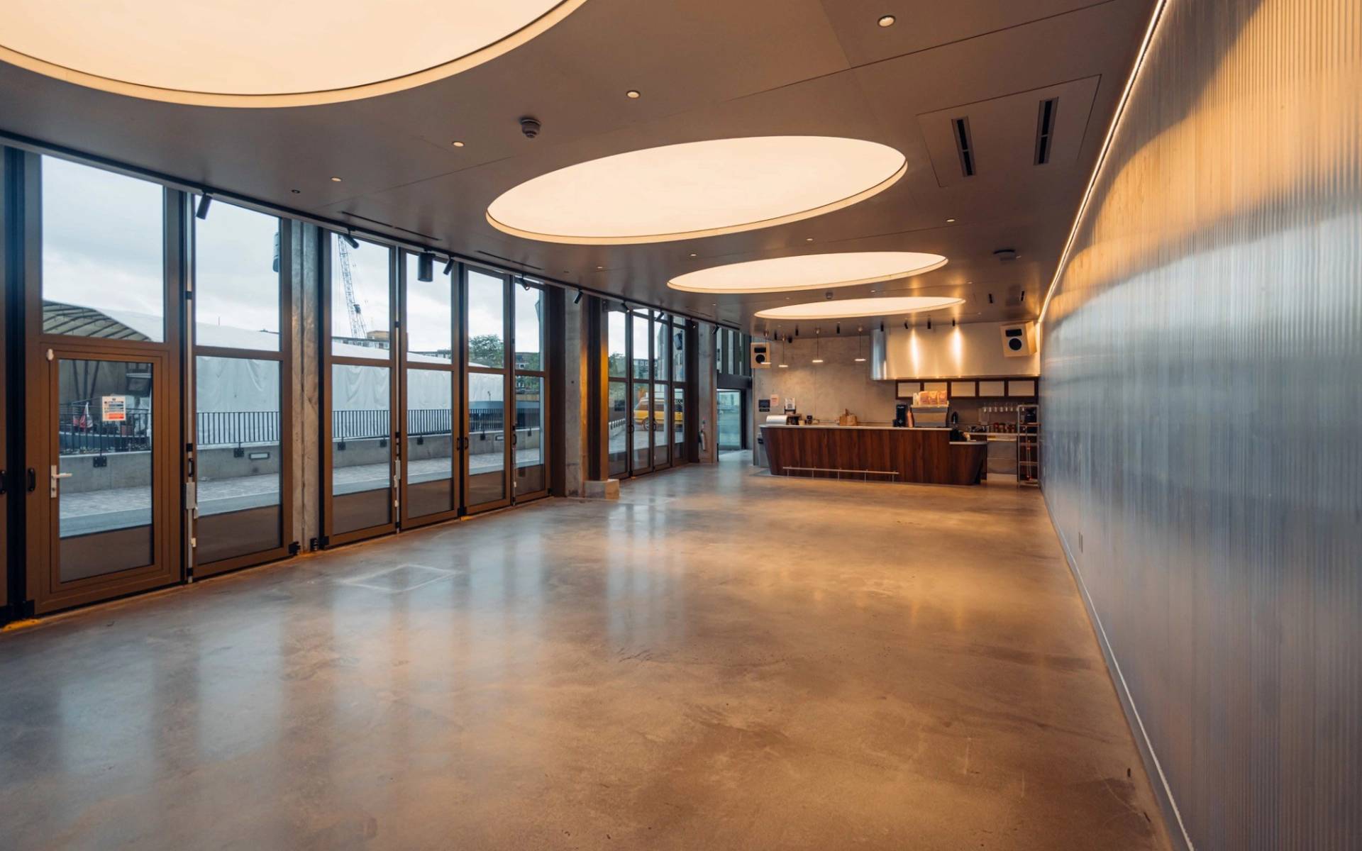 Bright open-plan venue space with large glass bi-fold doors and circular ambient ceiling lighting in Brentford TW8 via Love Locations.