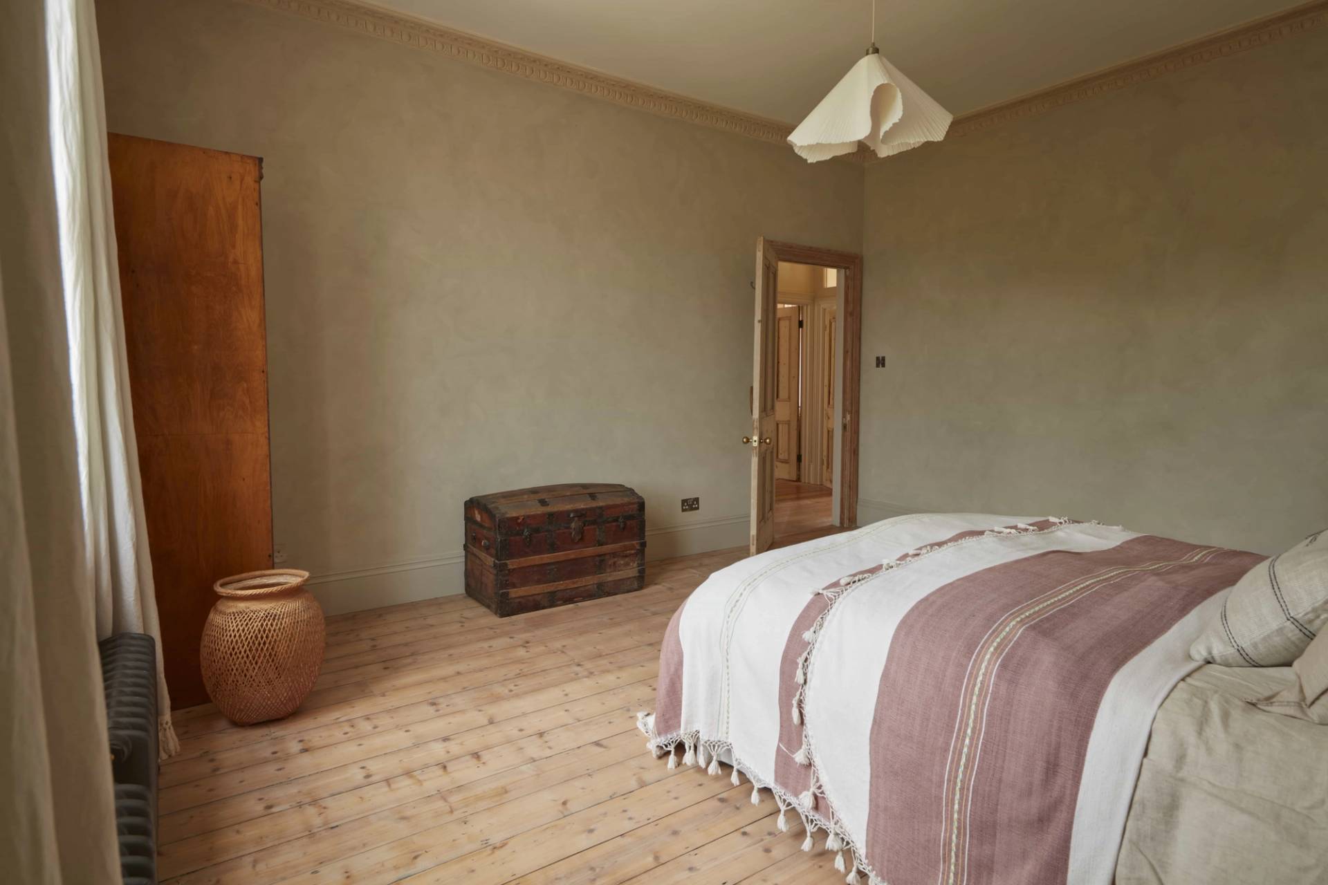 Spacious guest bedroom with plaster walls, vintage chest, and neutral bed linens, Love Locations.