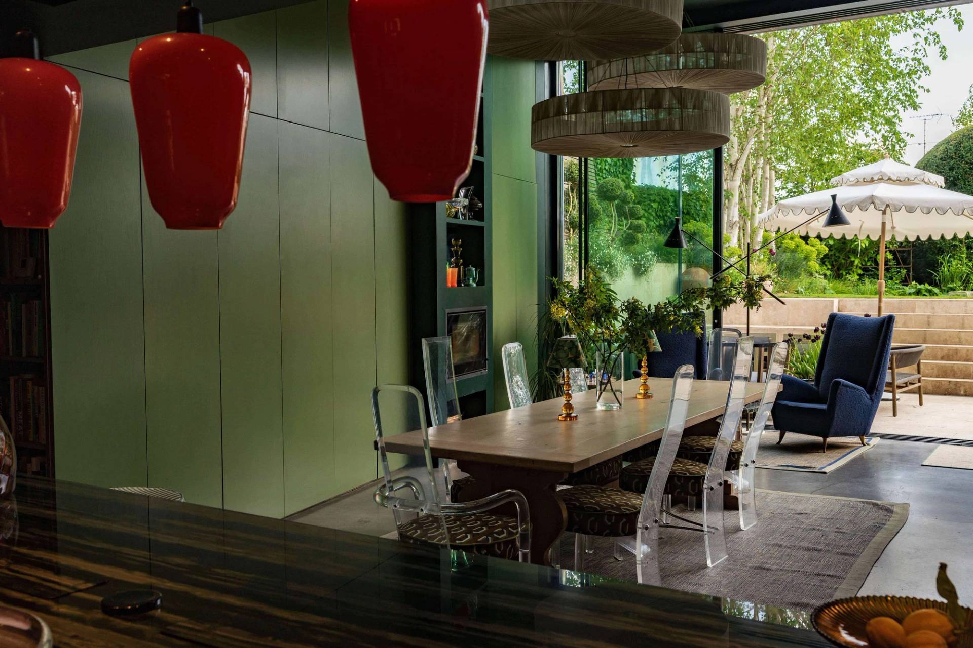 Formal dining setup in a double-height architectural extension featuring acrylic ghost chairs, wooden table, and red pendant light accents, Love Locations.