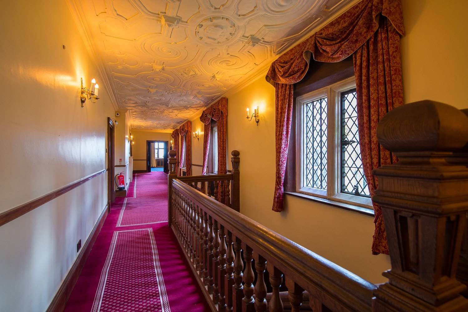 Sweeping period staircase and upper gallery landing with carved wooden balustrades and red runner carpet in Hertfordshire AL9 from Love Locations.