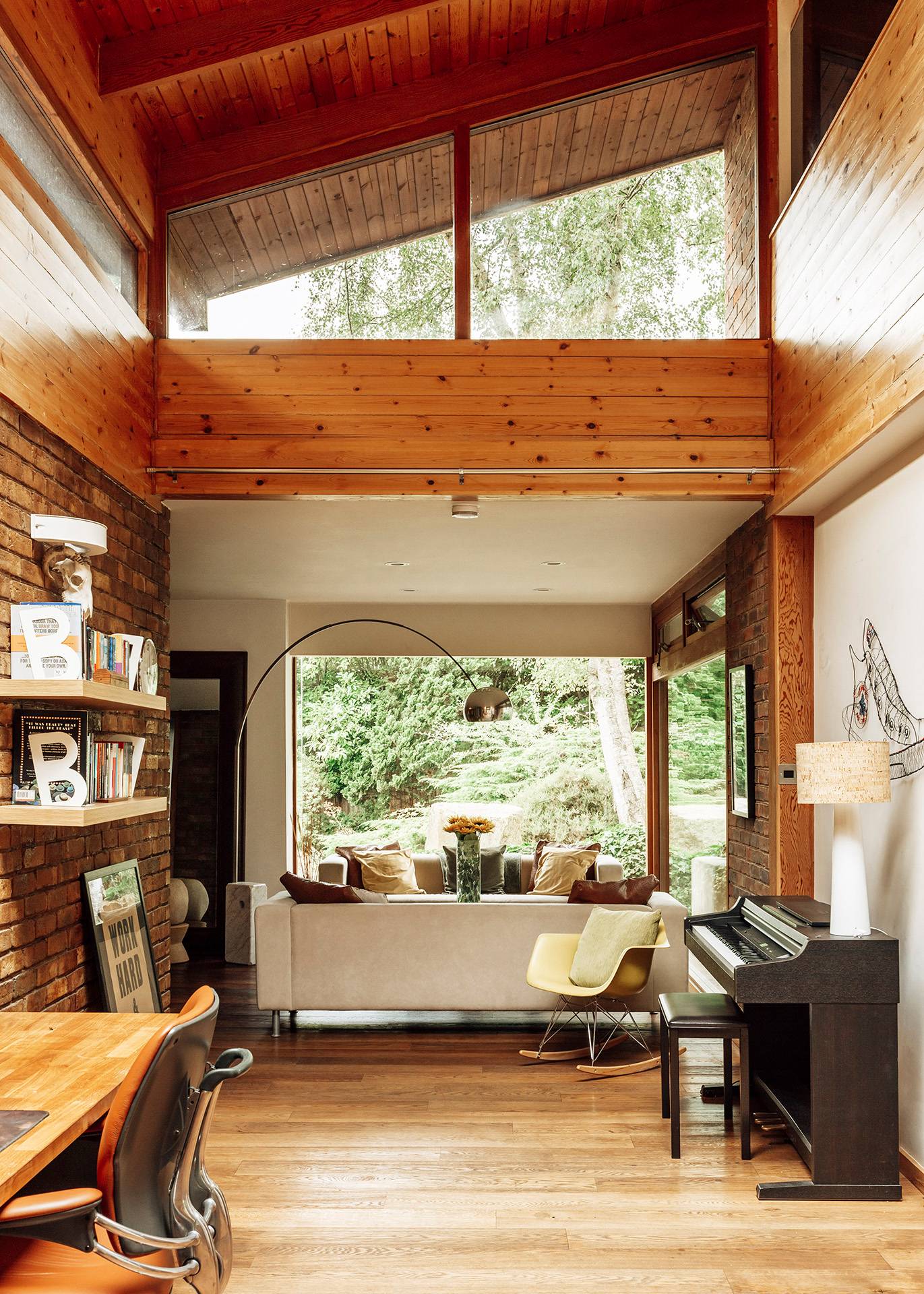 Mid-century open-plan study and music corner featuring a piano, bookshelves, and a large garden-facing window, Love Locations.