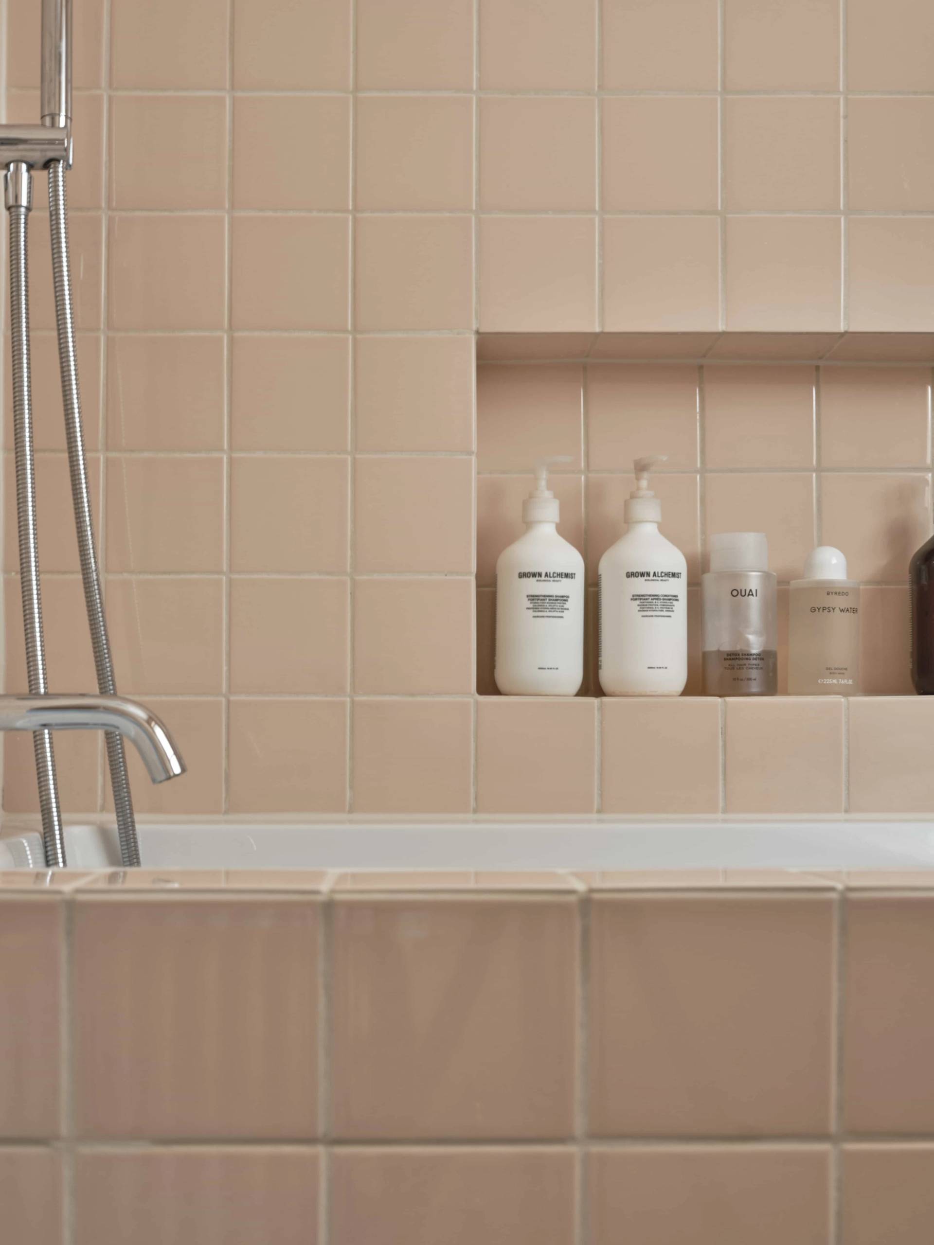 Close-up view of a built-in bathroom shower niche set in blush-pink square tiles with luxury toiletries, Love Locations E4.