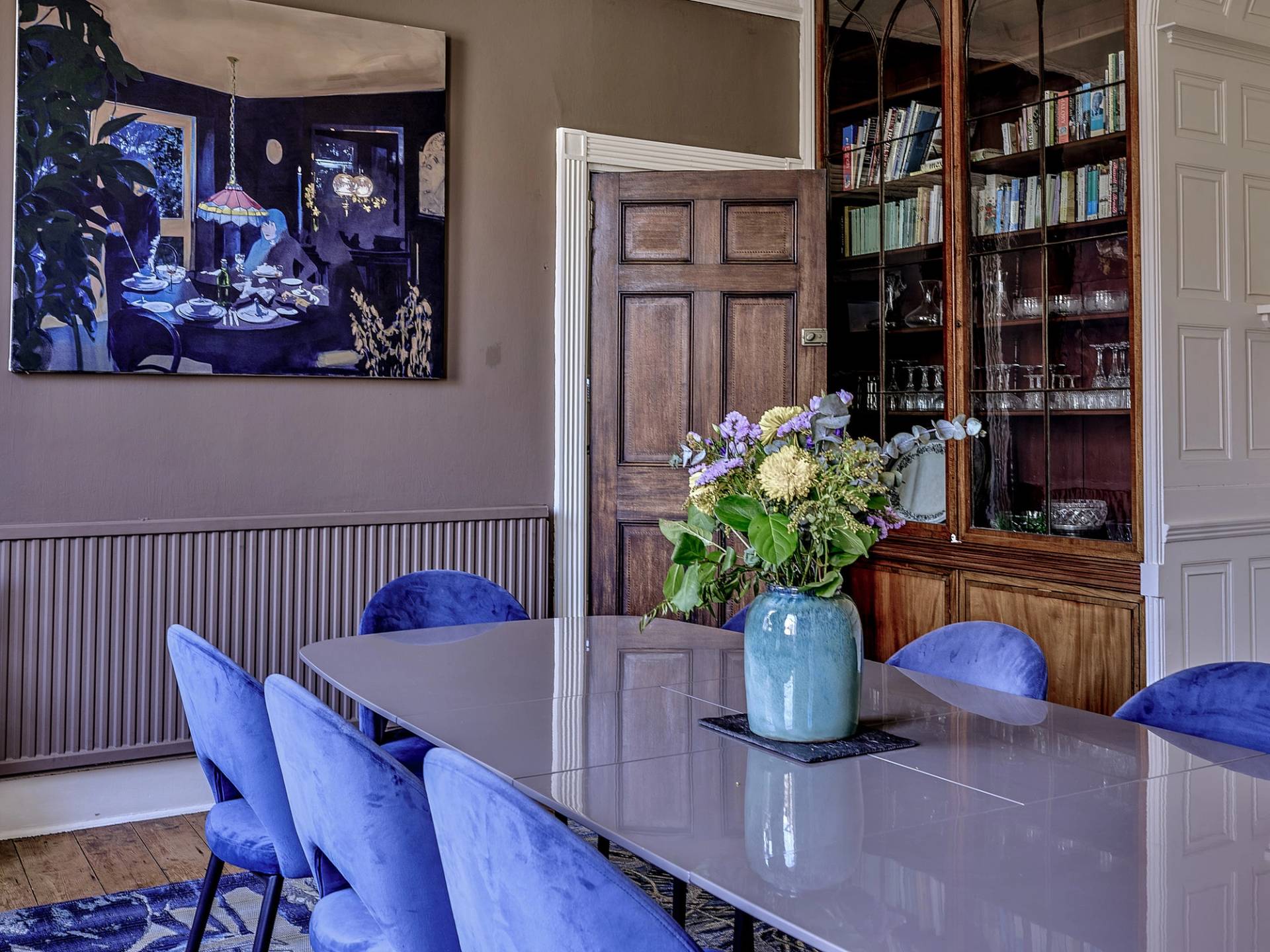 Formal dining space showing a dark wood bookcase, grey table, and blue velvet dining chairs, perfect for culinary TV ads, Love Locations ME13.