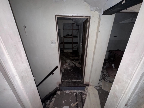 Looking through a dark doorway at the top of an old wooden staircase inside a boarded-up cottage, curated by Love Locations.