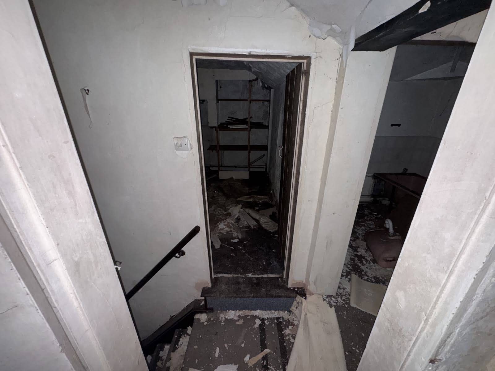 Looking through a dark doorway at the top of an old wooden staircase inside a boarded-up cottage, curated by Love Locations.