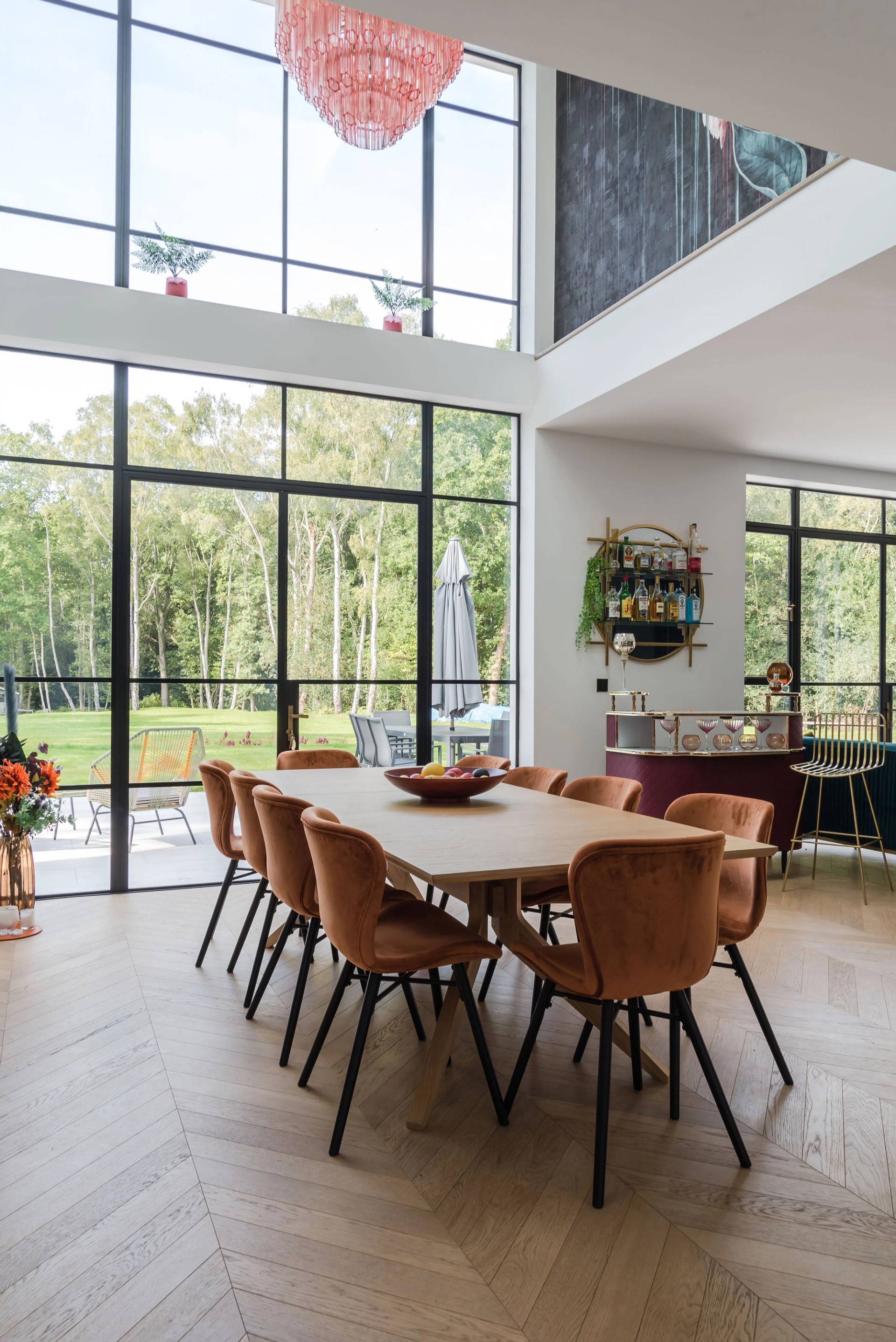 Double-height dining room with full-length crittall glass windows overlooking woodland, long dining table, and tan leather chairs, Love Locations GU3.