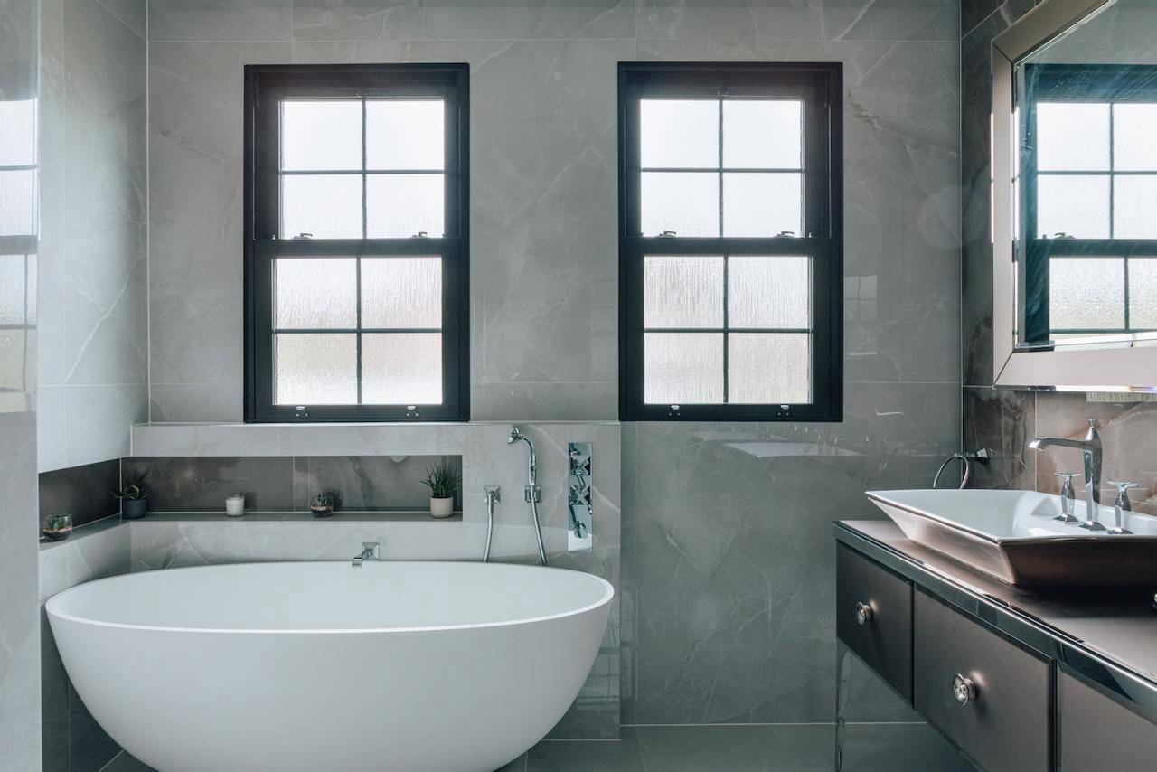 Modern grey bathroom suite with a freestanding oval tub, black window frames, and wall alcoves, perfect for spa and wellness ads, Love Locations W5.
