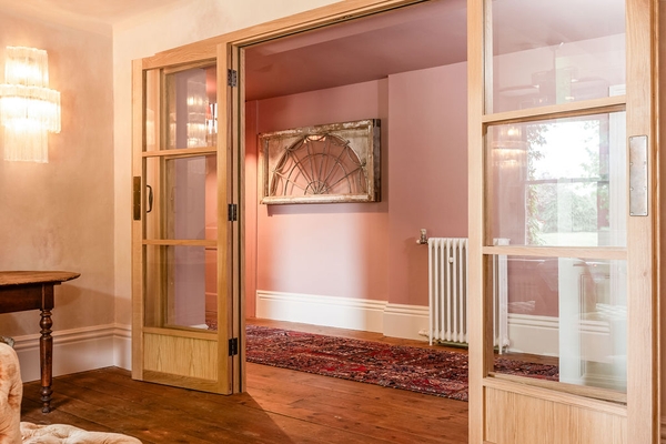 Historic country property hallway view framed by open timber glass doors leading into a pink-toned space from Love Locations.