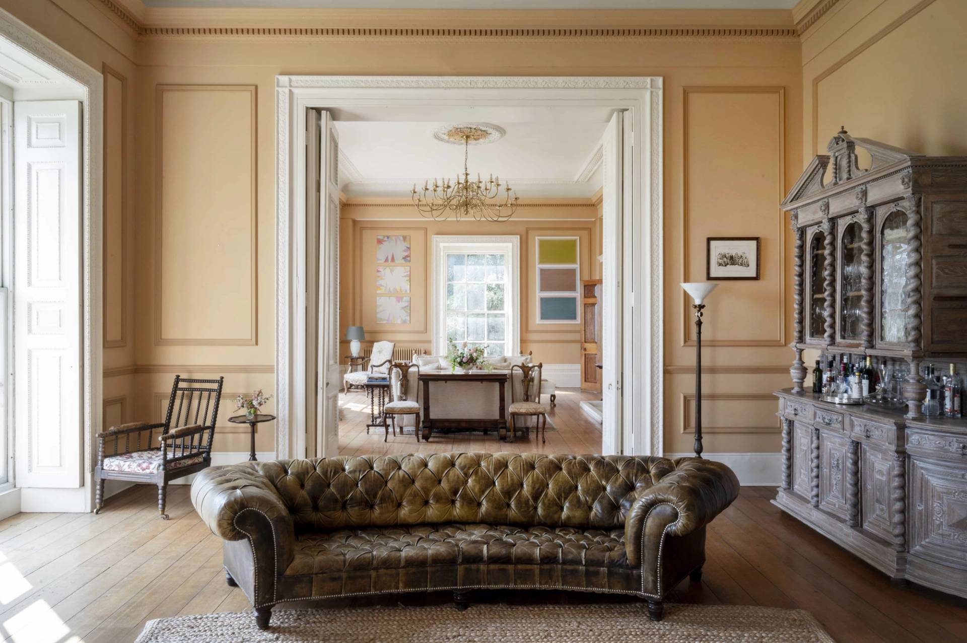 Enfilade view looking through double doors past a olive green button-tufted sofa into a light dining hall, Love Locations LE7.