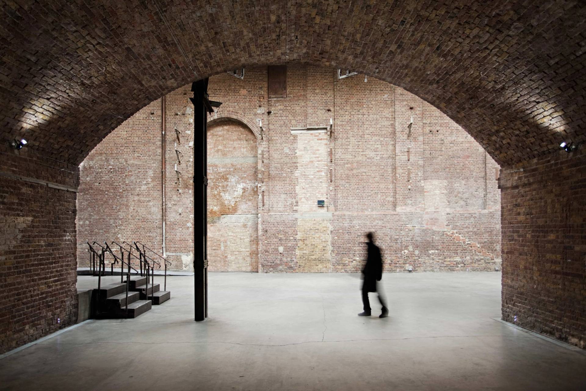 Atmospheric cavernous brick archway event space and live music venue in Hackney EC2A from Love Locations, featuring concrete flooring, silhouette lighting, and exposed brick walls.