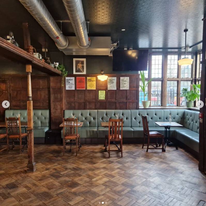 Traditional pub lounge film location in Lewisham SE6 from Love Locations, featuring green button-back leather banquettes, parquet flooring, and exposed ceiling ductwork.