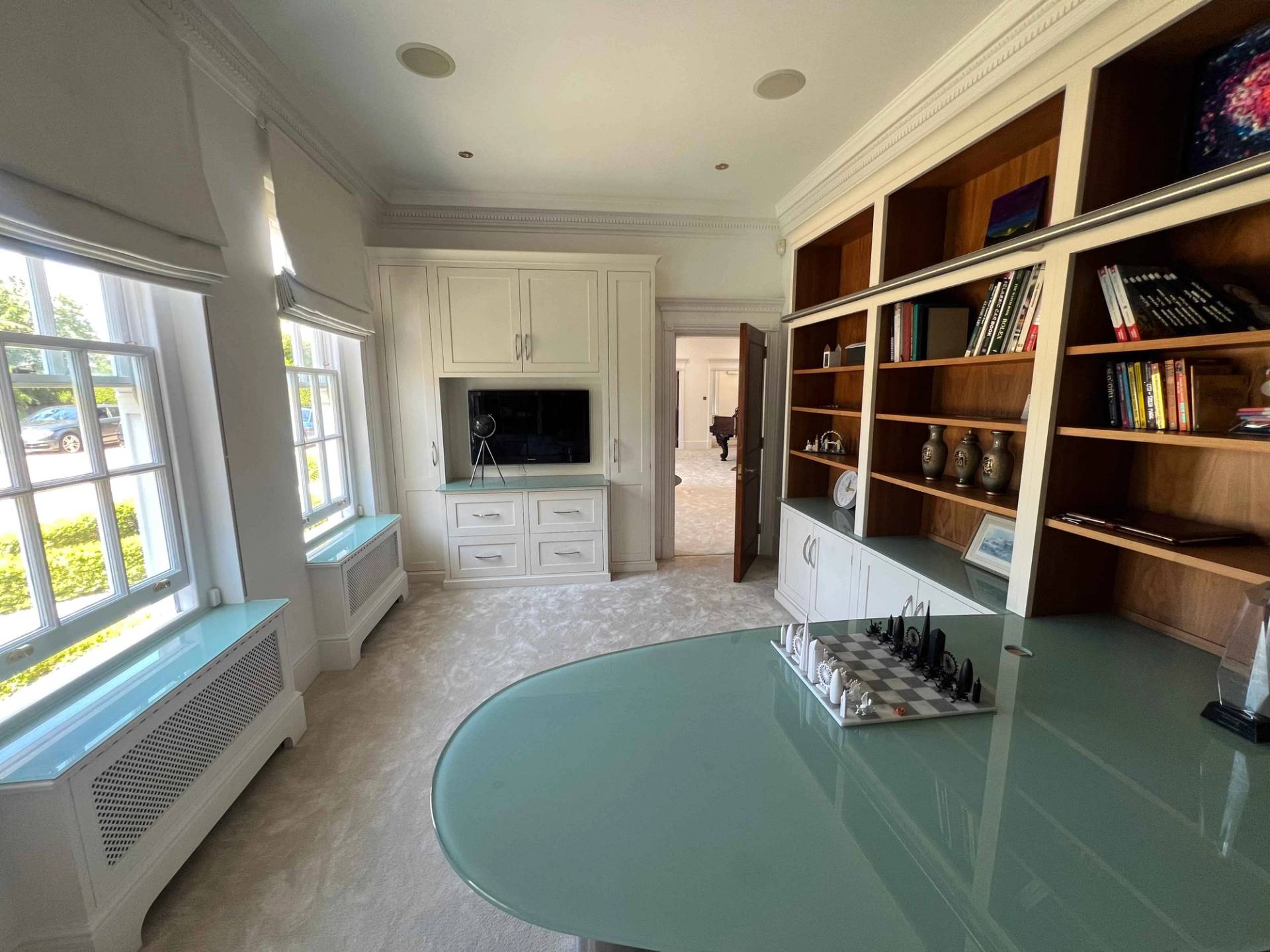 Executive home library featuring dark mahogany built-in bookcases, curved glass desk, and television, Love Locations BR7.