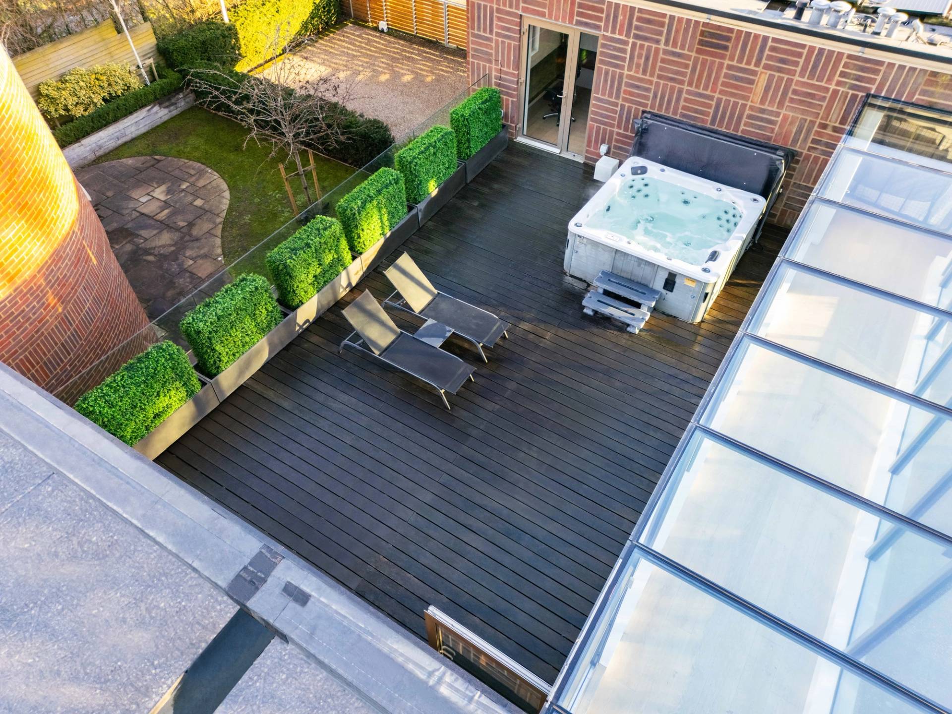 High-angle shot of a timber rooftop terrace with hot tub, sun loungers, and glass balustrades, Love Locations WD7.
