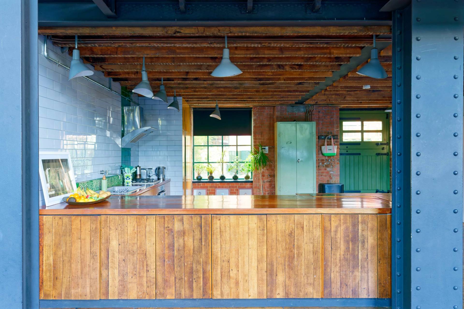 Close-up view of a thick timber kitchen island counter set against exposed brick walls and green pendant lighting, Love Locations E14.