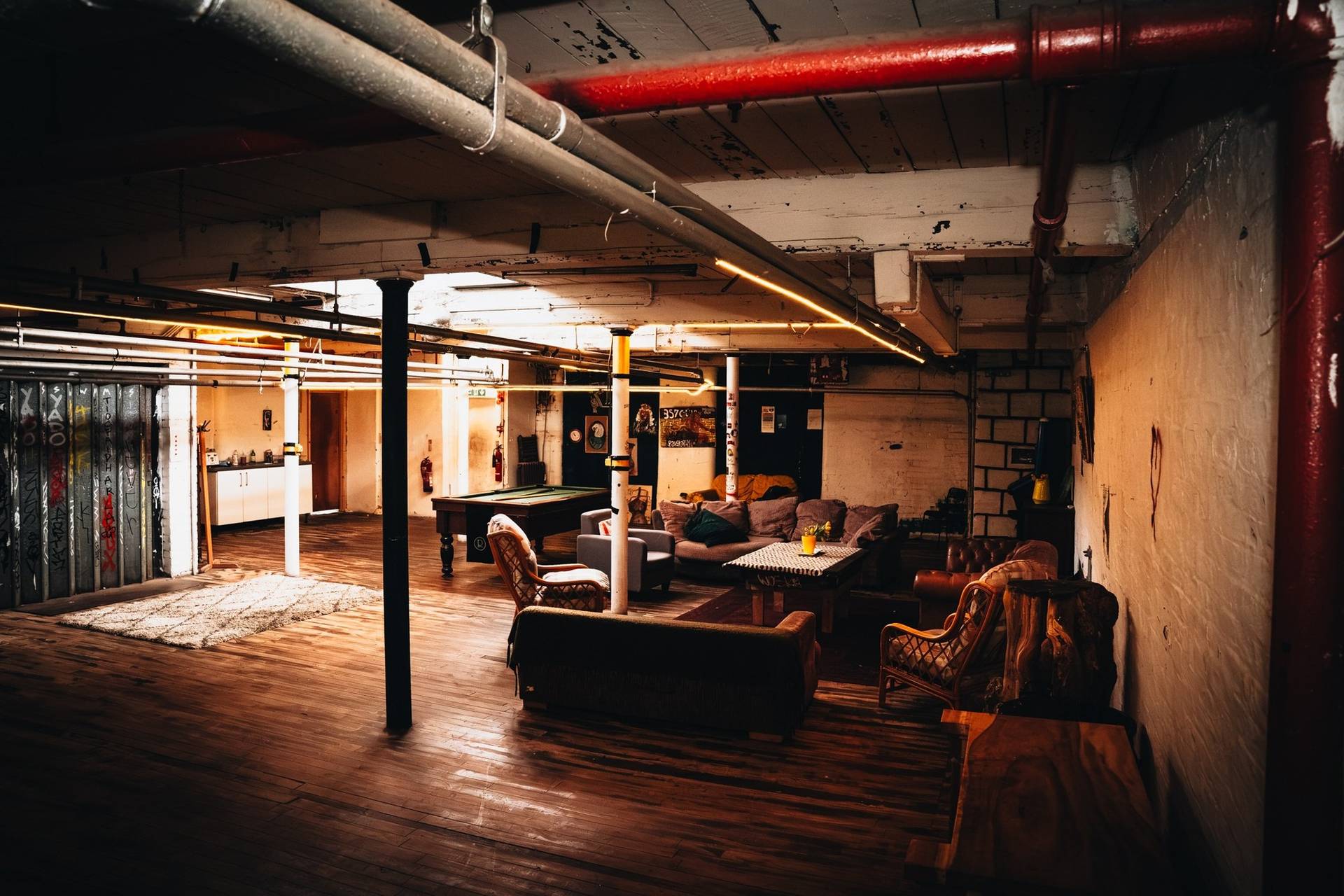 Industrial break-out lounge with pool table, leather couches, and overhead pipework in a Manchester M3 venue by Love Locations.
