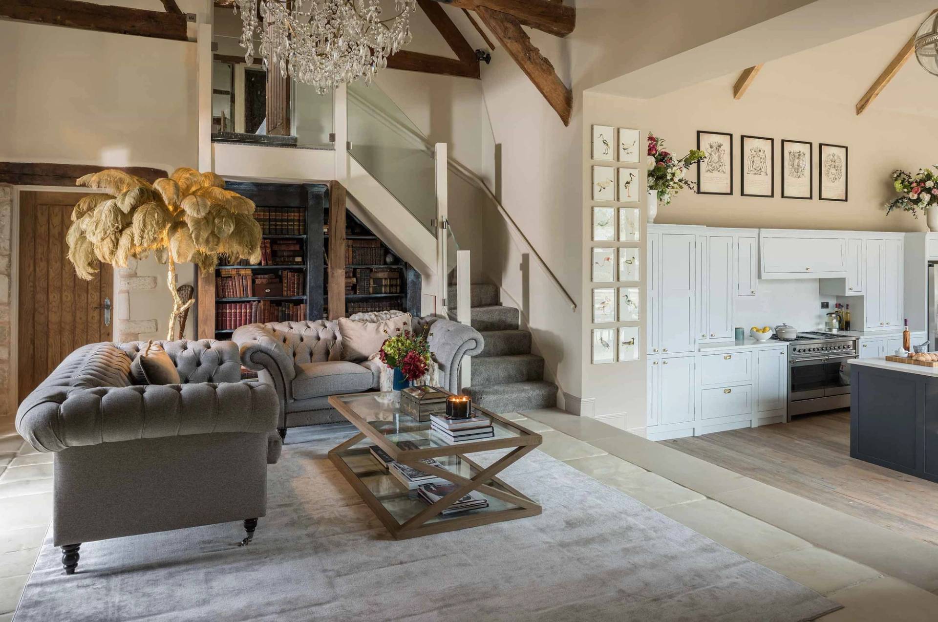 Architectural vaulted living room location home through Love Locations, displaying a glass-framed staircase, classic library shelving, and stone feature walls.