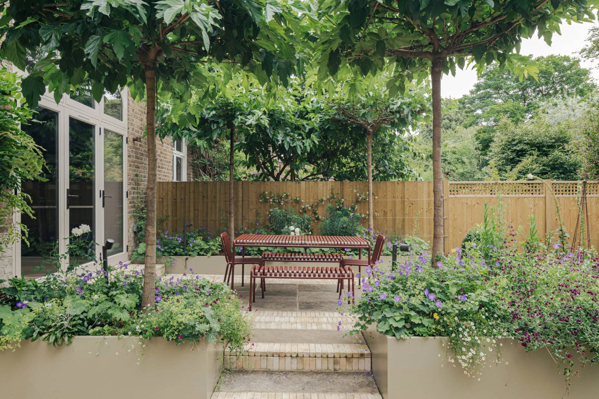 Formal garden patio with a red outdoor dining table set under pleached lime trees, perfect for summer lifestyle shoots, Love Locations SW13.