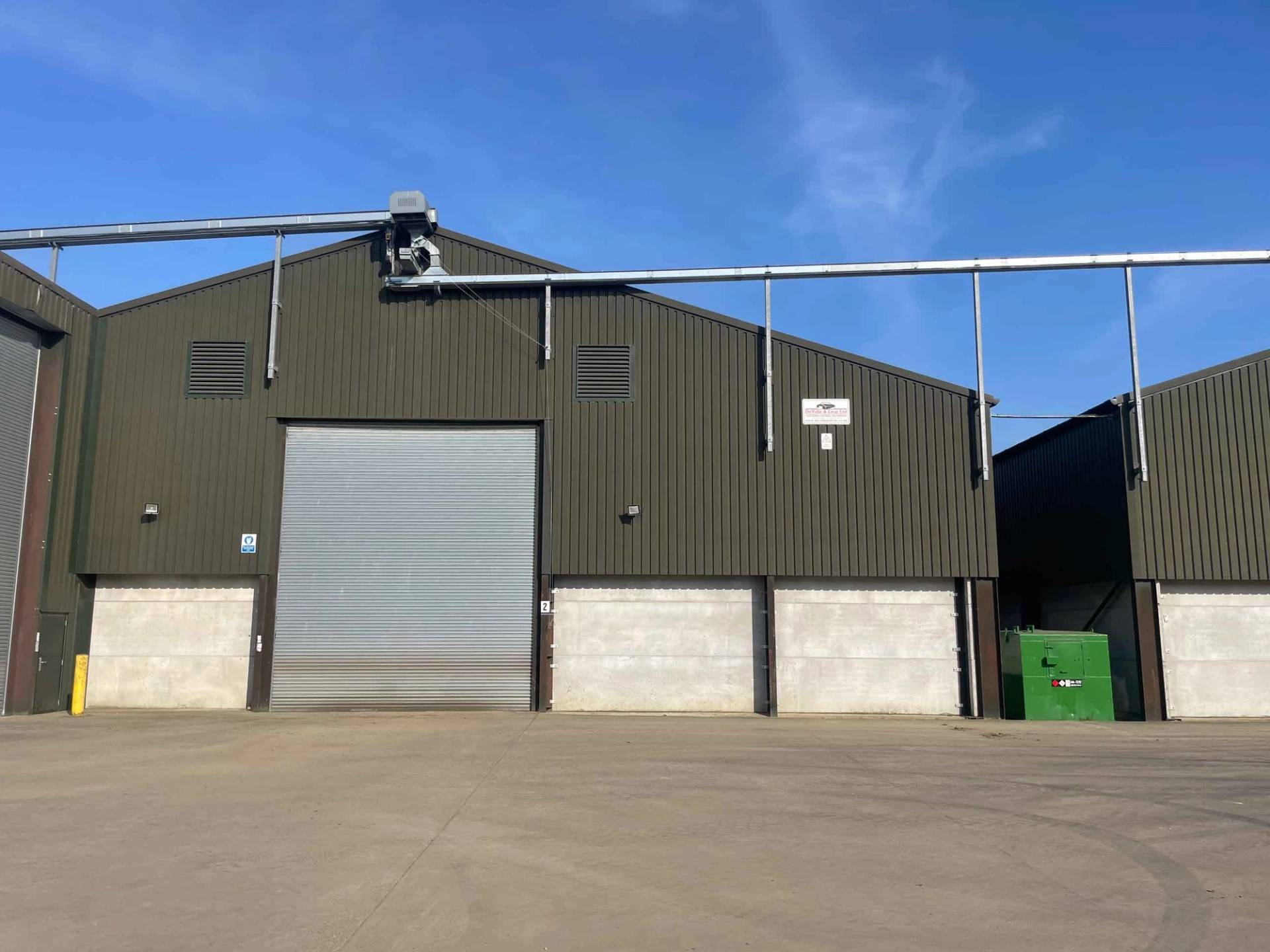 Modern green industrial agricultural warehouse with a secure roller door on a rural estate, Love Locations NN17.