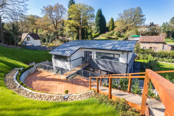 High-angle overview of a contemporary eco-house exterior showing extensive wooden decking and pristine surrounding woodland, Love Locations.