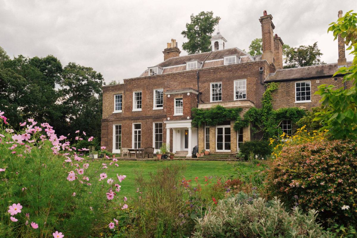 Side elevation view of a red brick Georgian estate surrounded by mature trees and lush green lawns, ideal for period drama filming, Love Locations SE15.