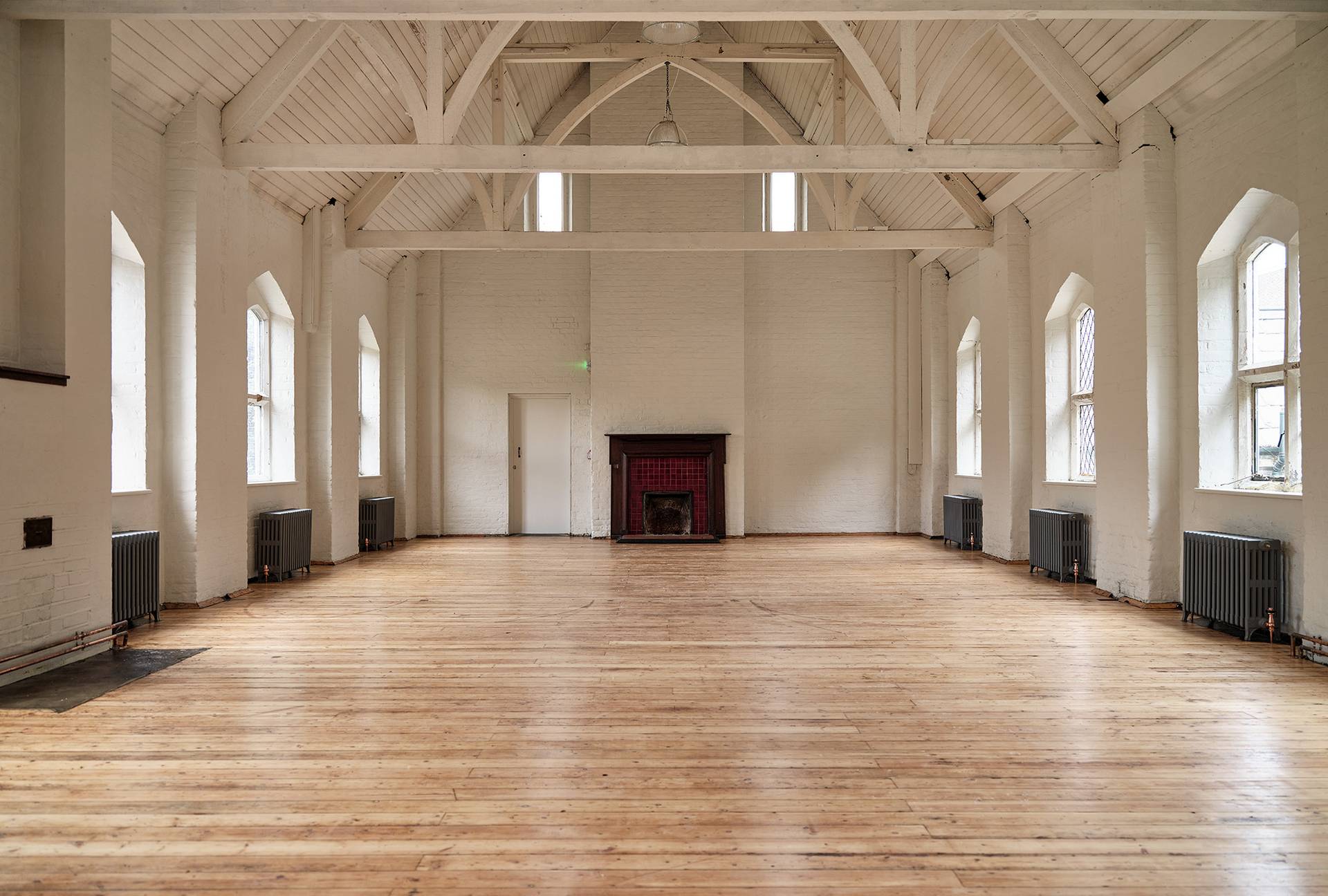 White painted vaulted hall with a dark green tiled fireplace hearth and polished wooden floorboards, Love Locations E2.