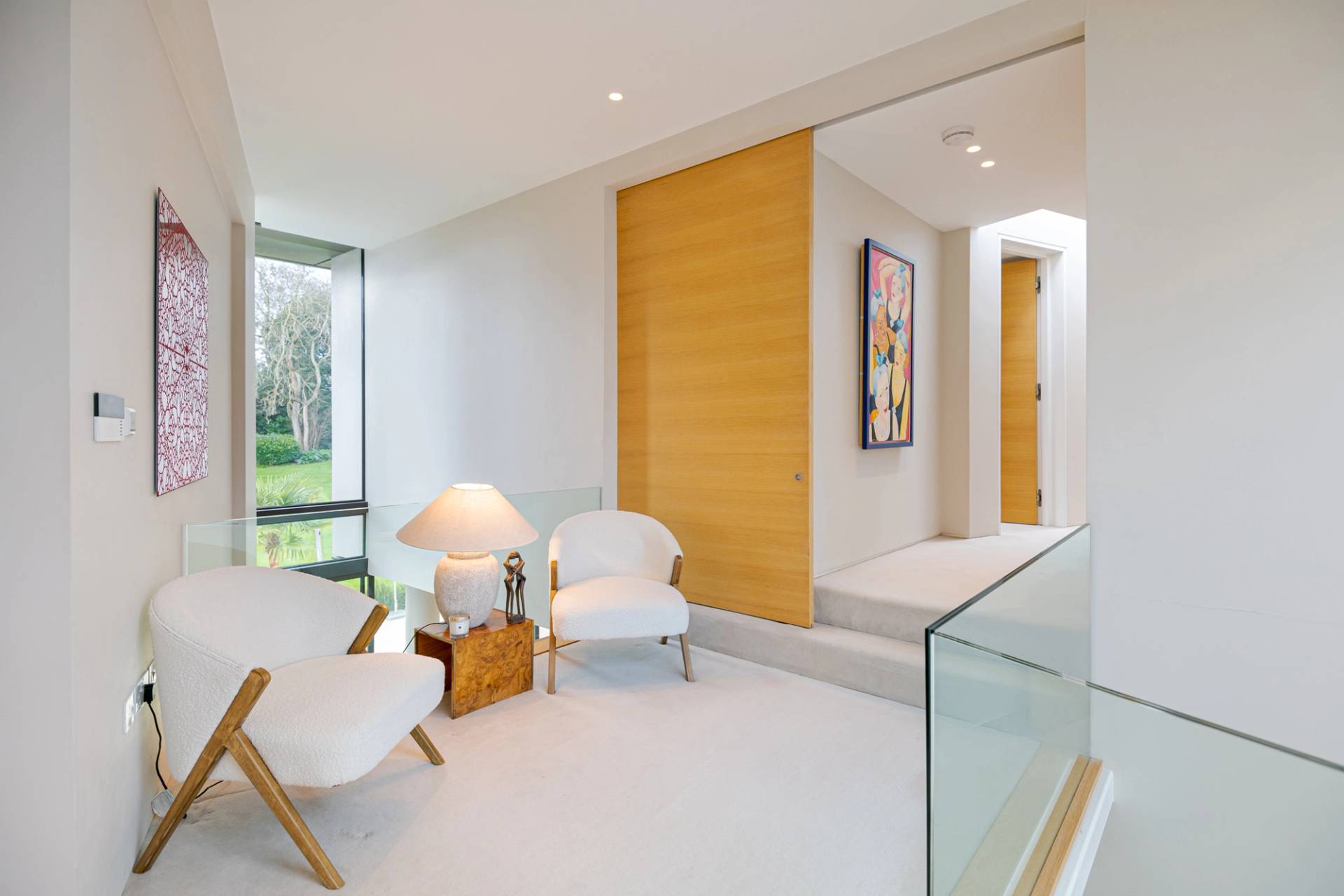 Modern upper floor landing transition with white armchairs, sliding timber doors, and picture window light, Love Locations KT2.