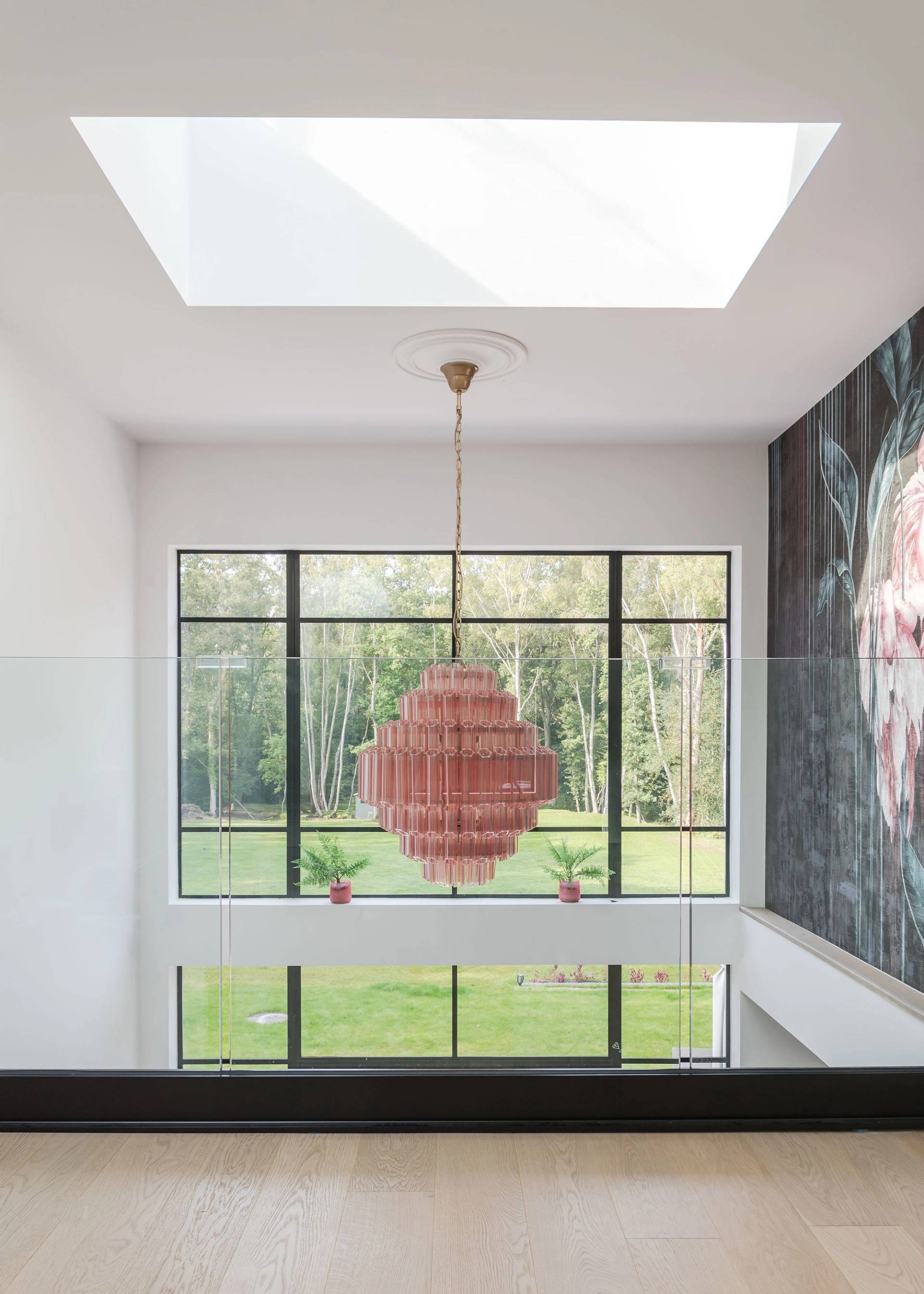 Double-height mezzanine landing featuring a dramatic pink fringed chandelier and large window framing forest views, Love Locations GU3.