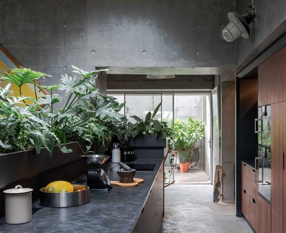 Industrial kitchen island prep space with dark composite counters, potted herbs, and brutalist concrete walls, Love Locations BN7.