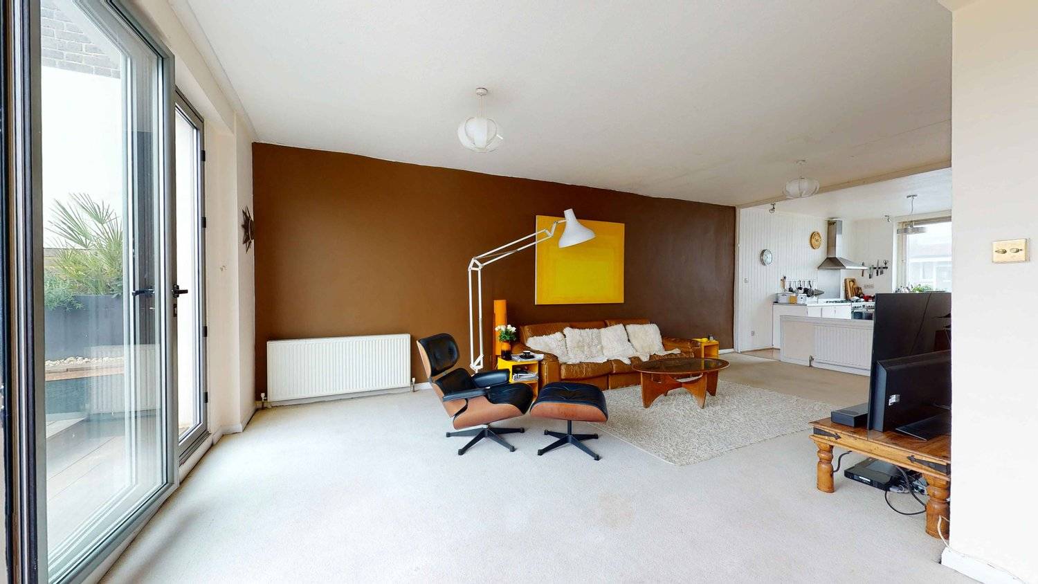 Retro living room setup featuring tan leather armchair with ottoman, floor-to-ceiling windows, and white carpet, Love Locations SW16.