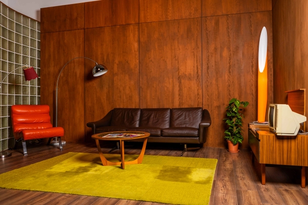 Retro 70s studio set in Tottenham, N15 with timber wall panelling, dark leather sofa, chartreuse carpet, and indoor plant, Love Locations.