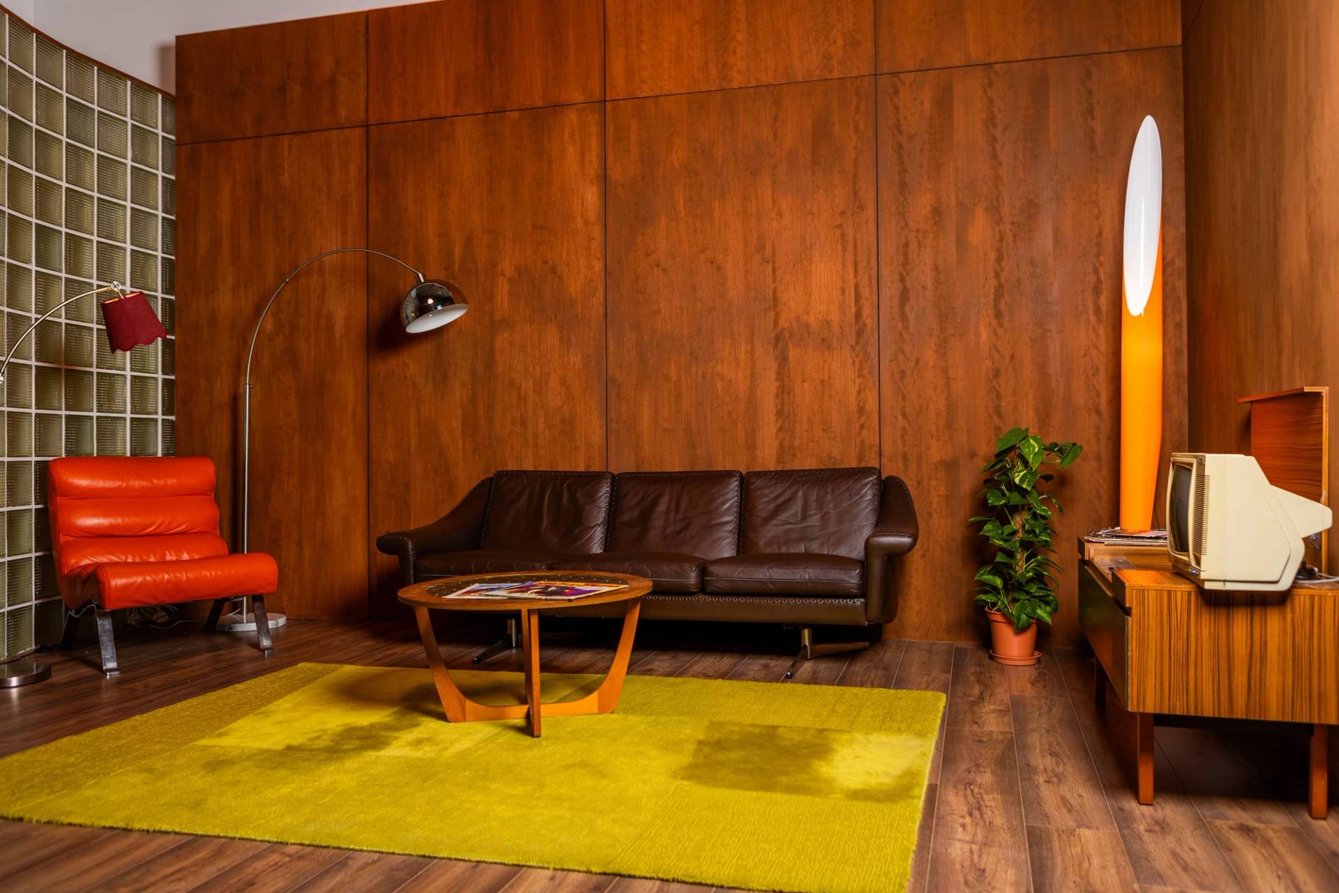 Retro 70s studio set in Tottenham, N15 with timber wall panelling, dark leather sofa, chartreuse carpet, and indoor plant, Love Locations.