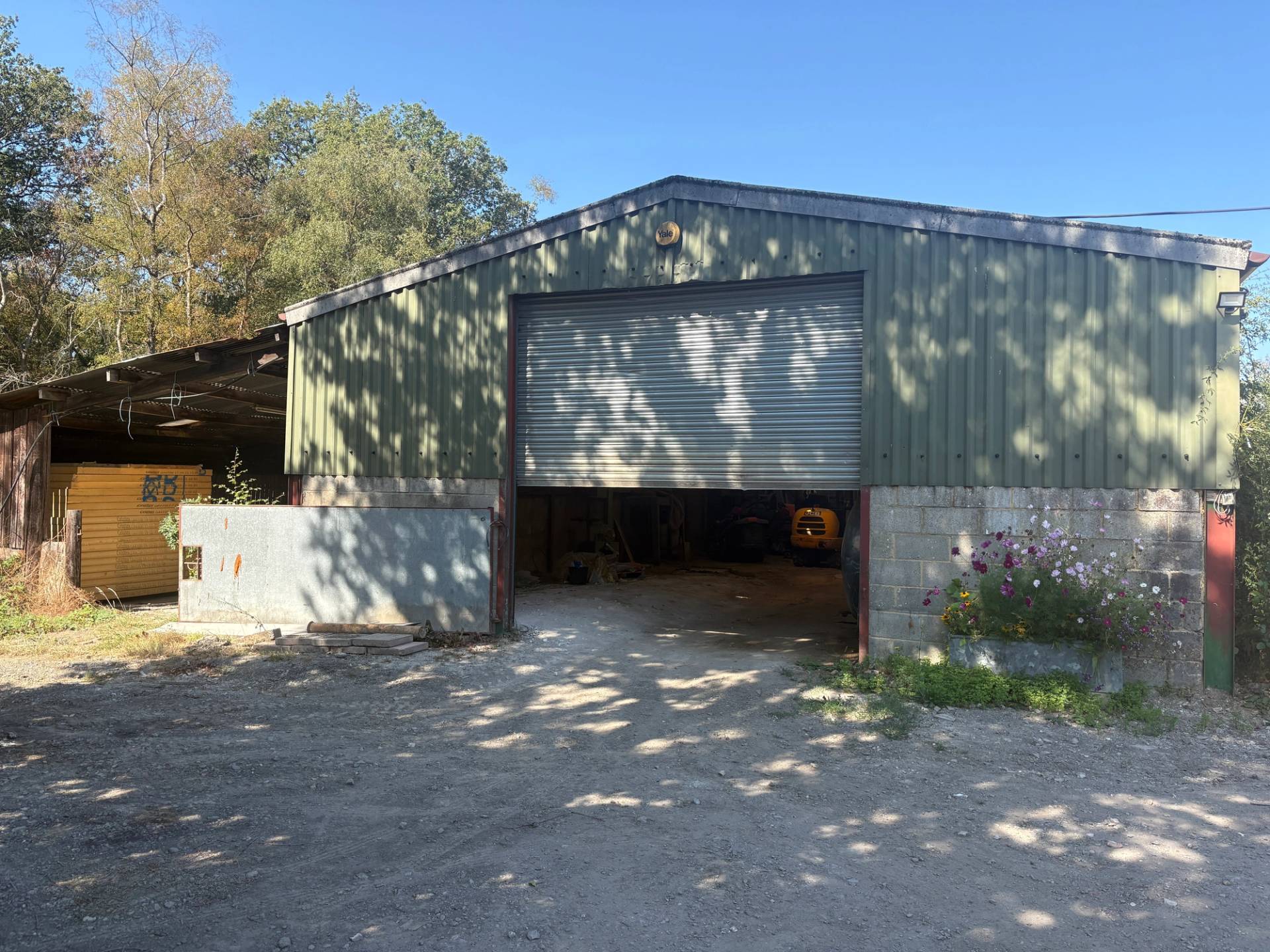Green corrugated metal industrial barn facade with open roller shutter door and concrete forecourt yard in South Chailey, Love Locations BN8.