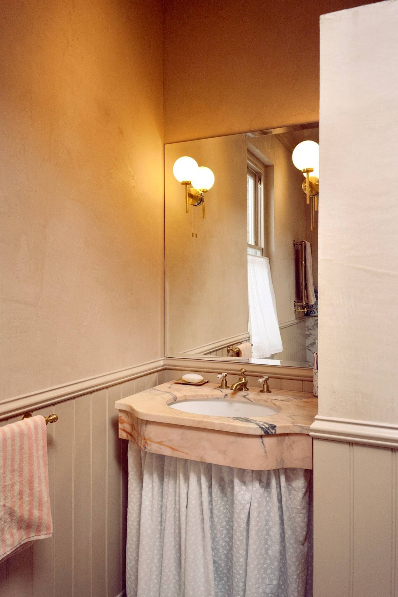 Classic guest bathroom vanity area featuring a skirted sink unit and a large illuminated wall mirror, Love Locations Hounslow.