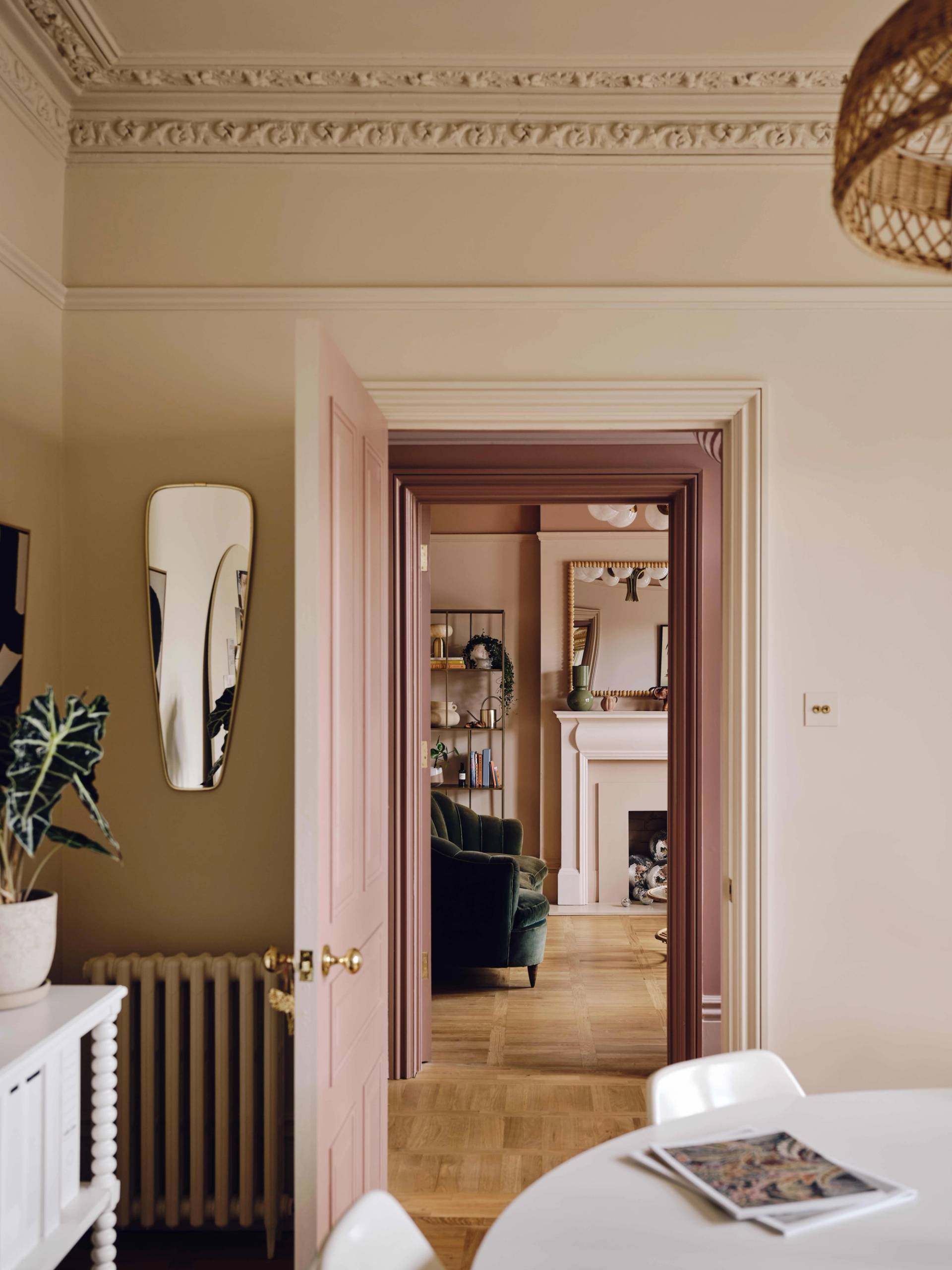 Off-white dining room view framed through pink doorways with a round dining table and sash window light, Love Locations CR0.