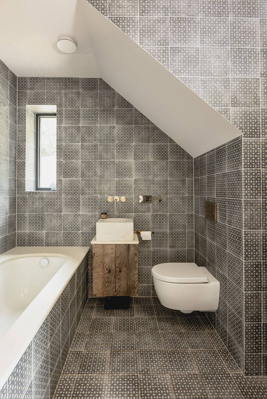 Contemporary bathroom featuring dark grey wall tiles, glass shower, floating toilet, and wood vanity, Love Locations GU32.