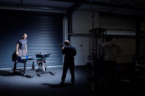 Behind-the-scenes view of a commercial video production crew filming inside an industrial gym unit with dramatic lighting near a roller shutter door, Love Locations.
