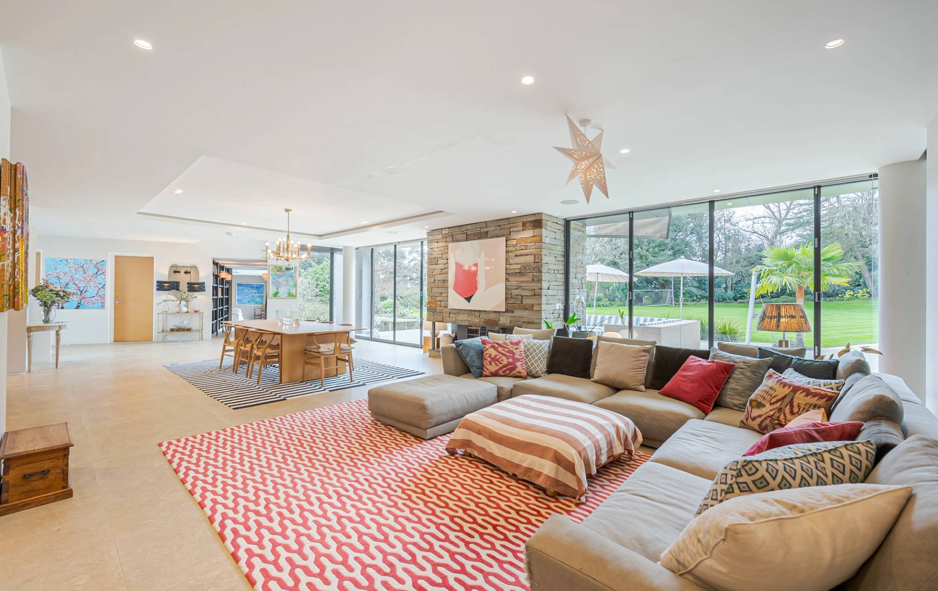 Spacious family lounge room featuring an L-shaped beige sofa, red chevron rug, and floor-to-ceiling glass looking out onto garden grounds, Love Locations KT2.