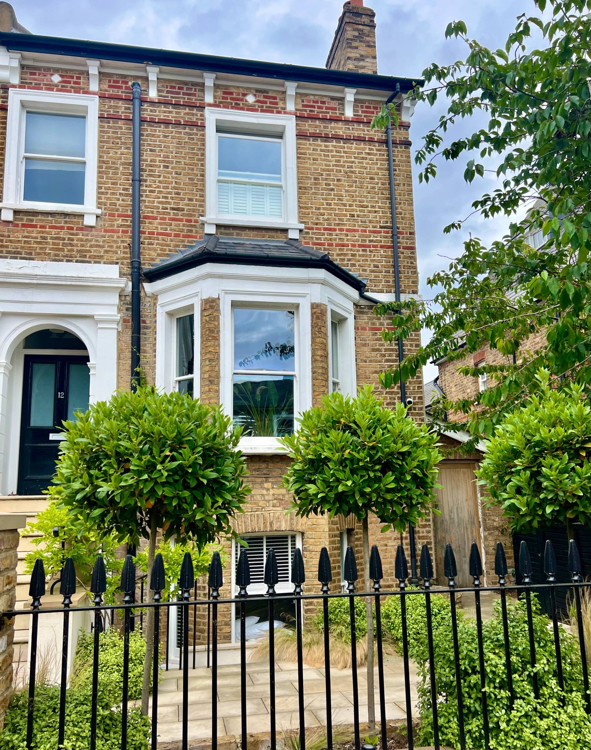 Victorian location house hero cover image in Twickenham, TW1 featuring a red brick bay-fronted facade, modern double-height glass extension, reclaimed wood kitchen island, floating timber stairs, outdoor garden pond, and private gym outbuilding, the ultimate high-visibility backdrop for feature film productions, TV drama filming, commercial brand campaigns, and editorial photography via Love Locations.